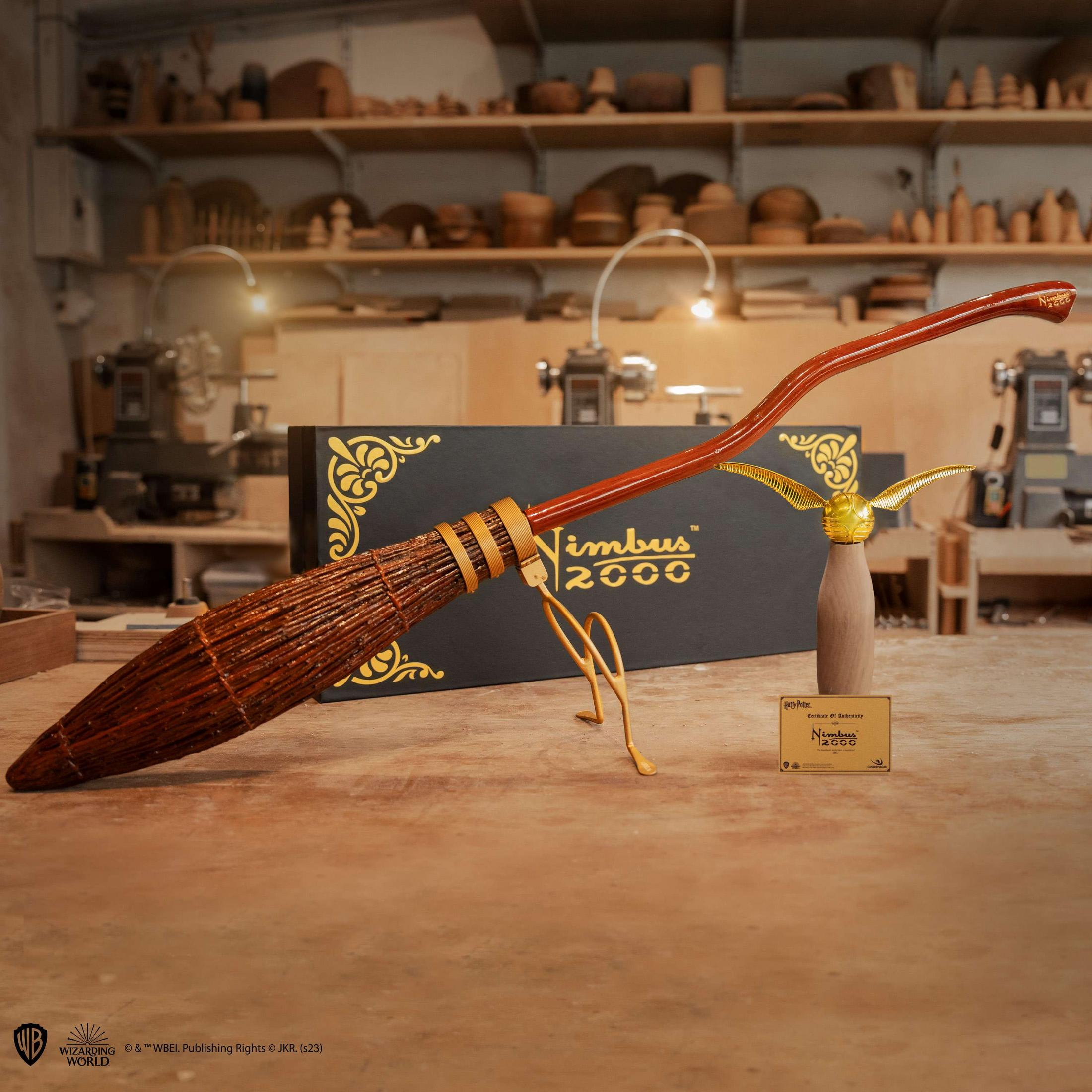 Ein Nimbus 2000 Besen liegt auf einem Holztisch, mit einem goldenen Schnatz daneben.