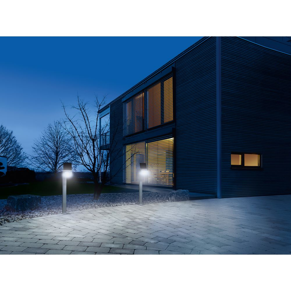 Zwei moderne Außenleuchten beleuchten einen gepflasterten Weg vor einem Haus bei Nacht.