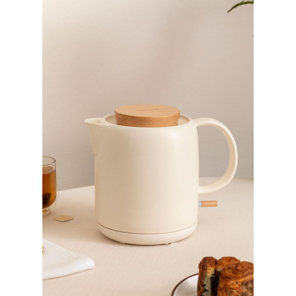 Una tetera color crema con tapa de madera sobre una mesa.