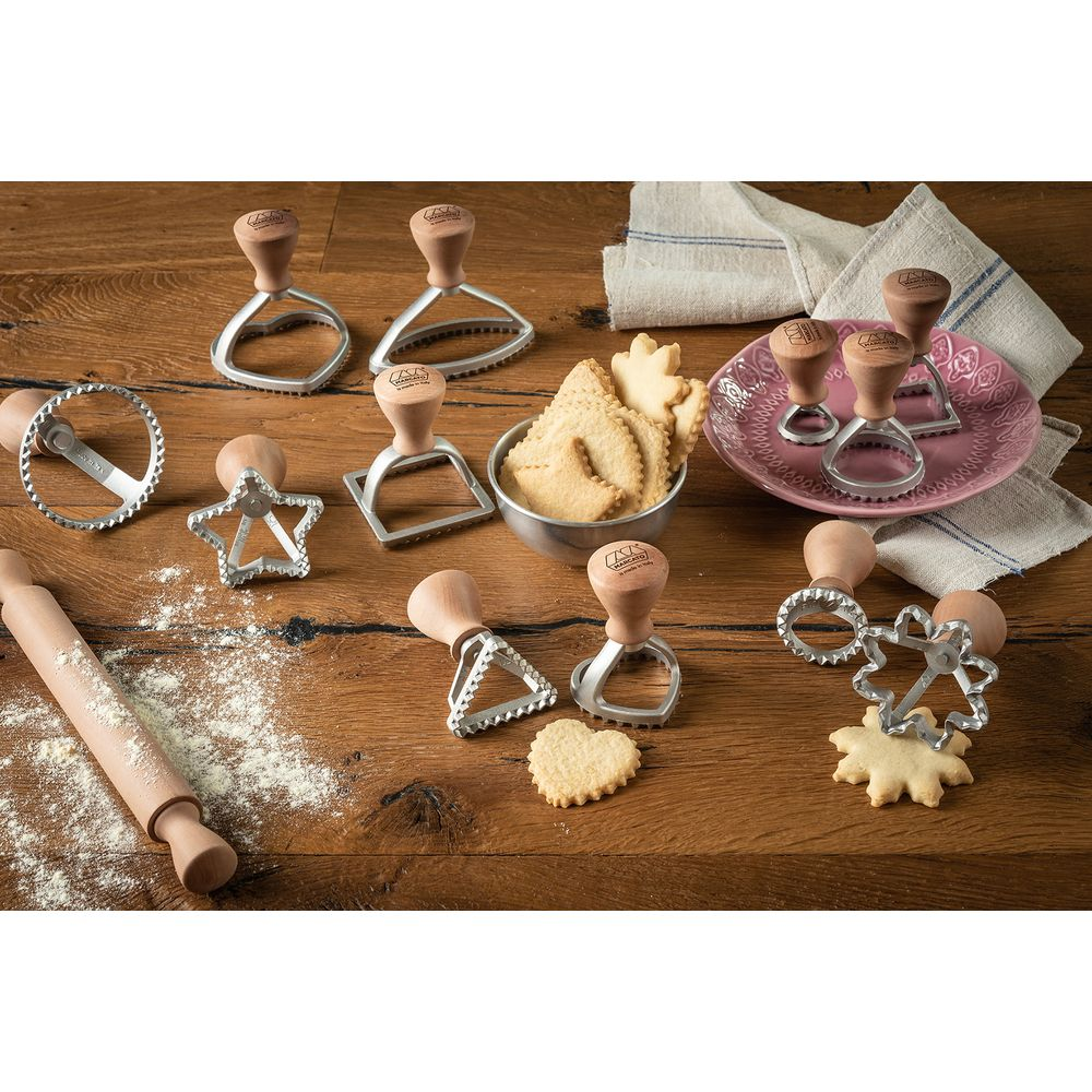 Emporte-pièces à manche en bois de formes variées sur table en bois avec farine et biscuits.