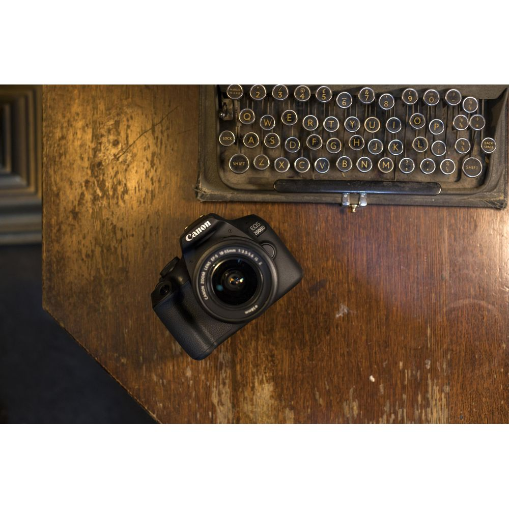 Eine schwarze Canon EOS 2000D Kamera liegt auf einem Holztisch neben einer alten Schreibmaschine.
