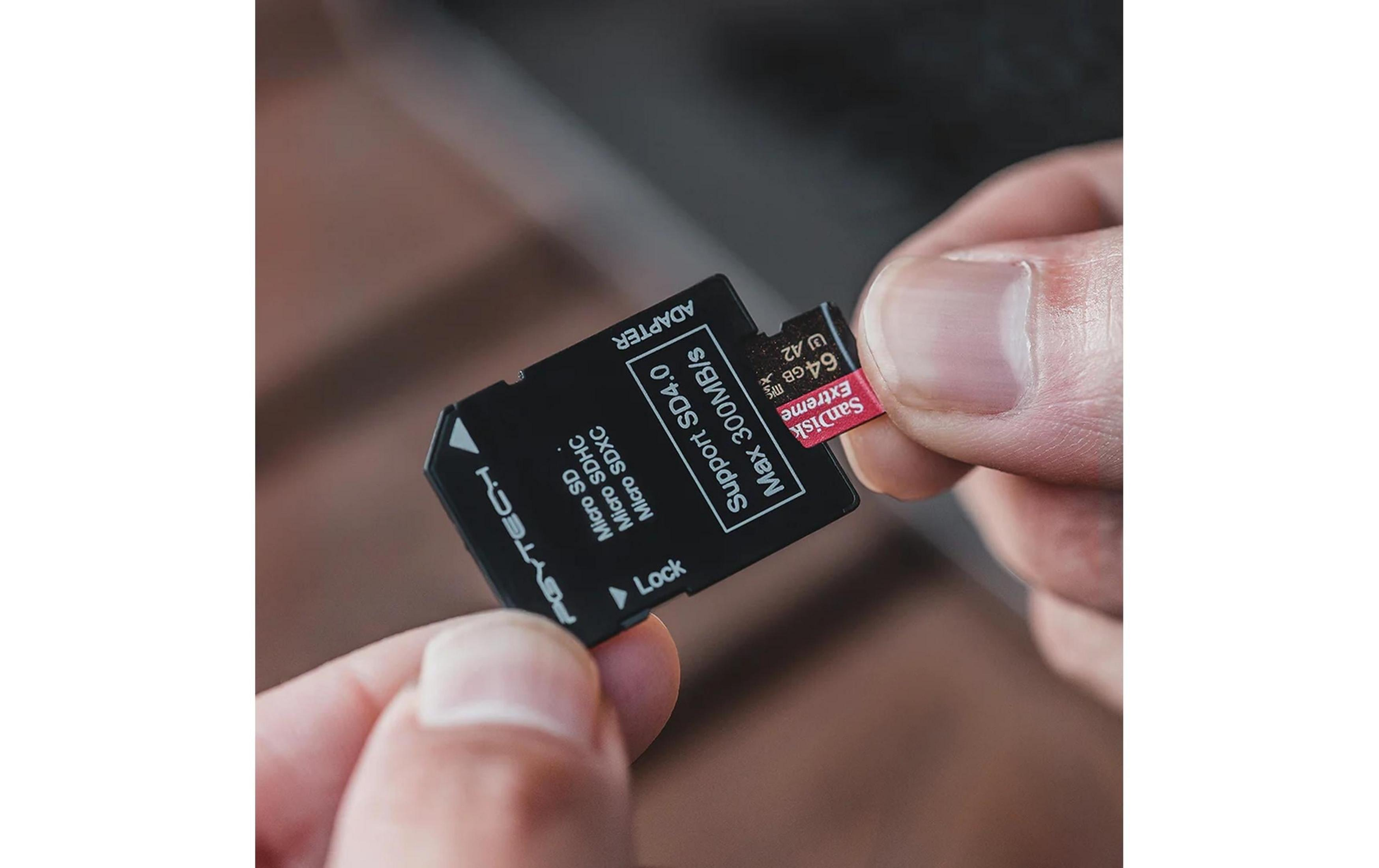 Dłoń wkłada czerwoną kartę micro SD SanDisk Extreme 64GB do czarnego adaptera.