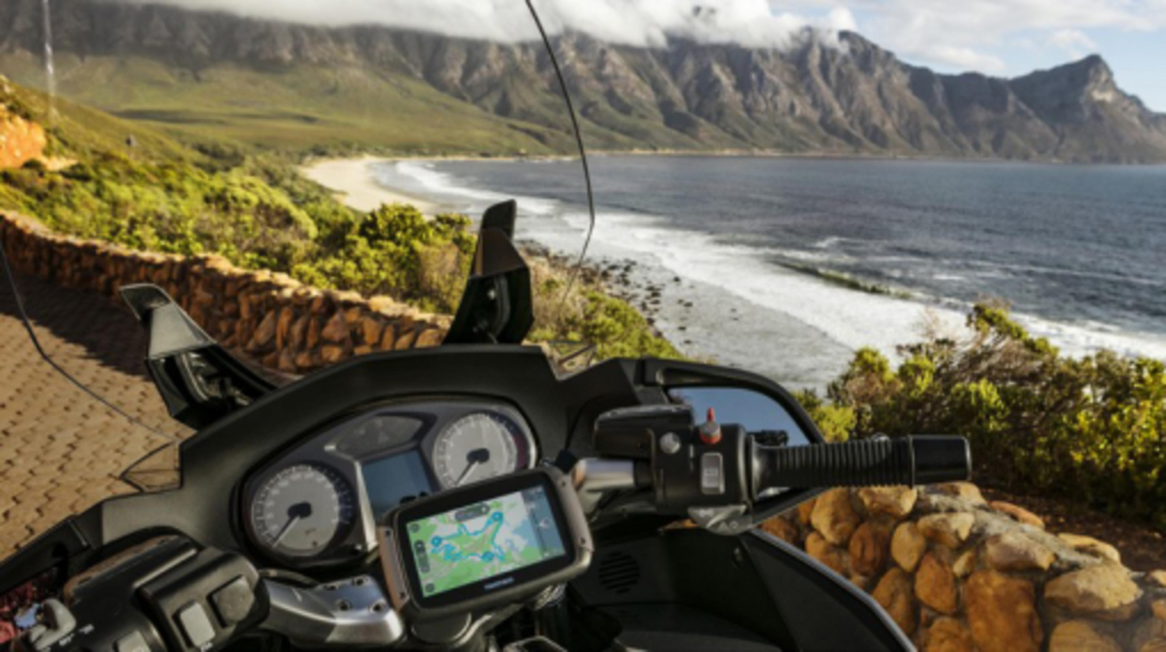 Motorrad-Armaturenbrett mit GPS an malerischer Küstenstraße mit Blick auf Berge und Meer.