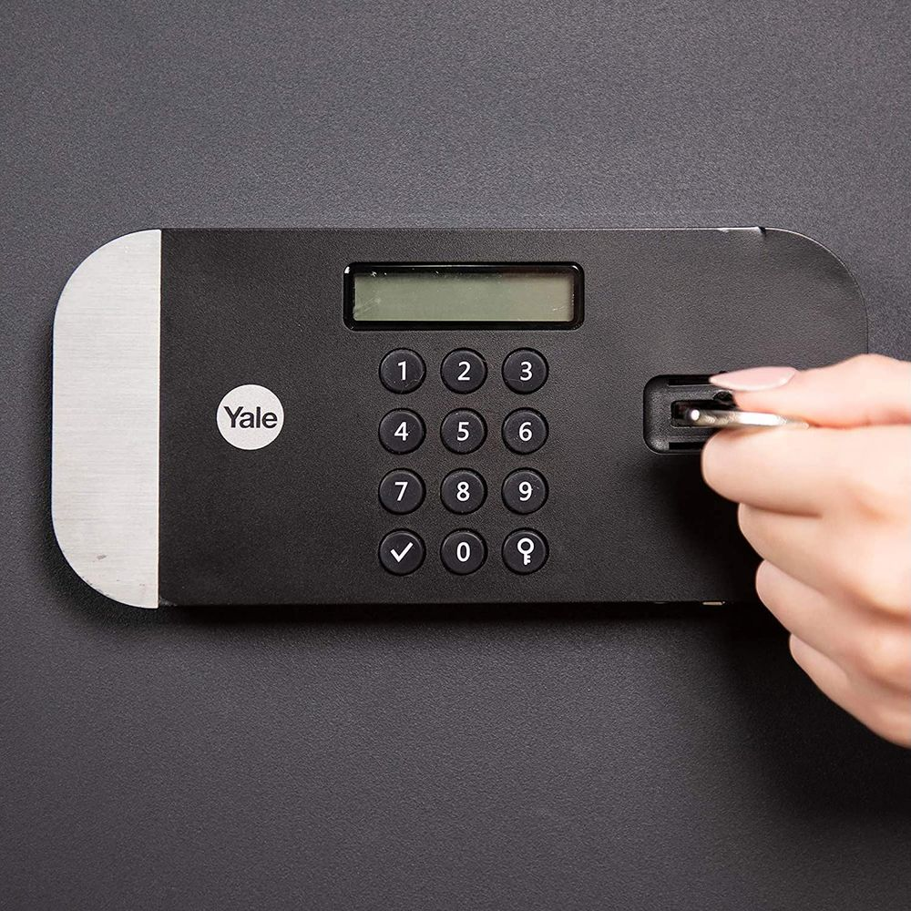 Una mano introduce una llave en una cerradura de teclado Yale en una puerta negra.