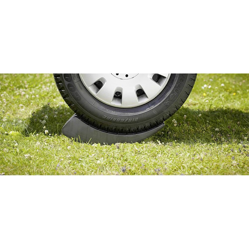 Uno pneumatico per auto poggia su un cuneo nero sull'erba verde.
