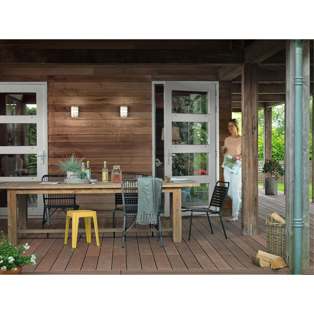 Holzterrasse mit Tisch, Stühlen und einer Frau, die ein Magazin hält.