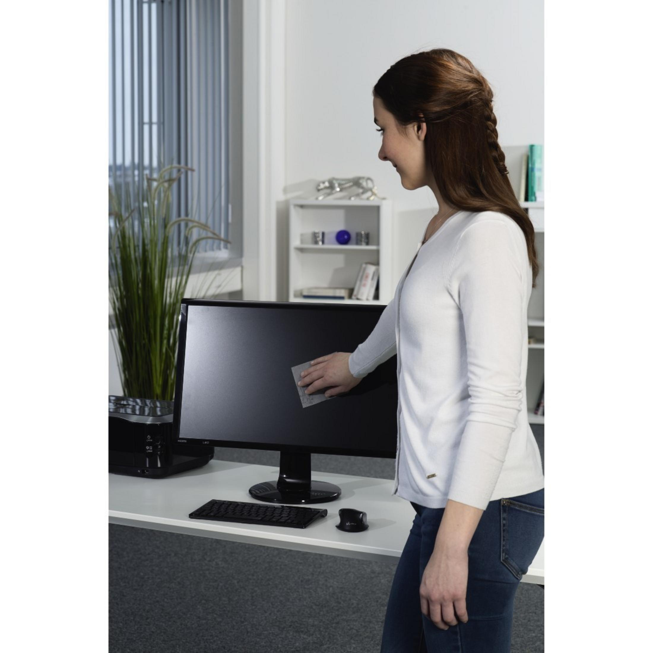 Frau wischt Monitor mit Tuch ab, Schreibtisch mit Tastatur und Maus.