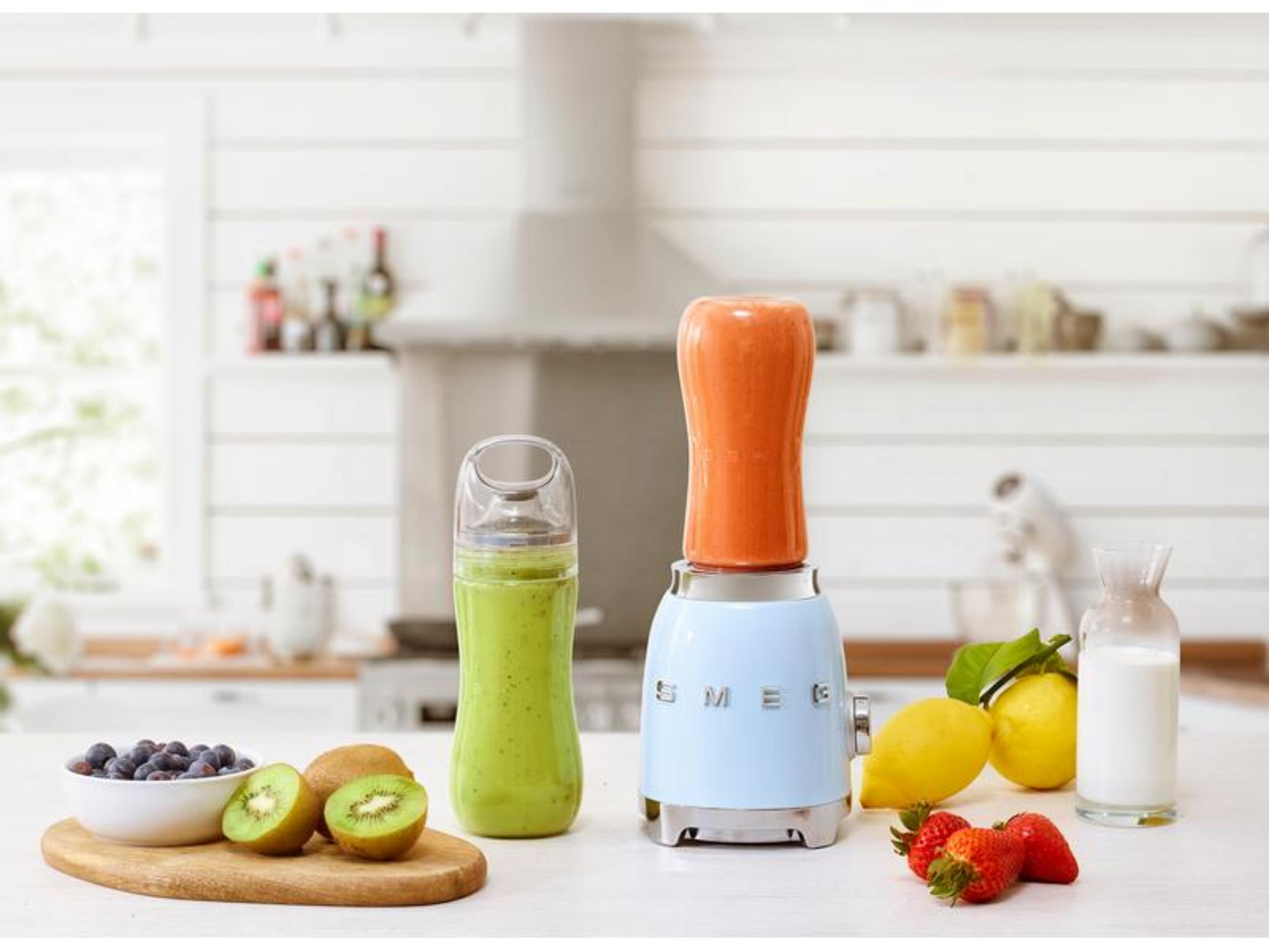 Niebieski blender z pomarańczową nasadką obok szklanki zielonego smoothie.