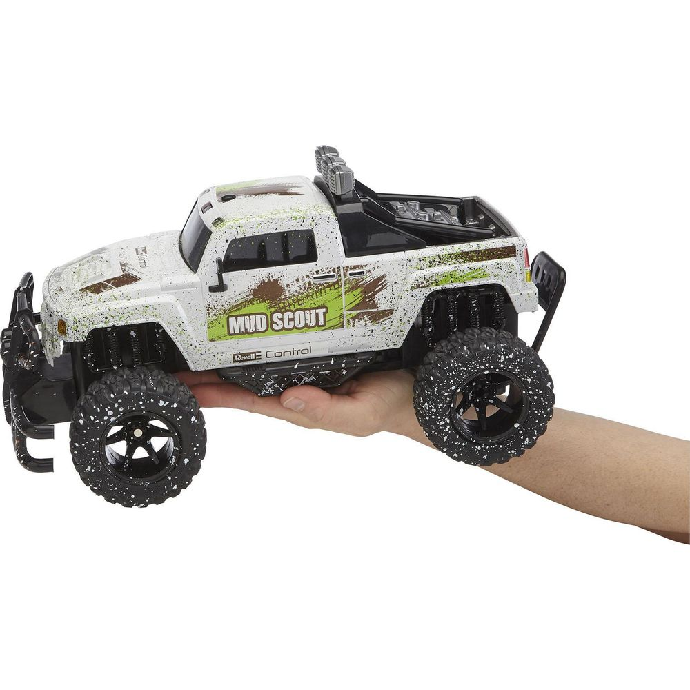 Ein weißer ferngesteuerter "Mud Scout"-Truck mit großen Reifen wird in einer Hand gehalten.