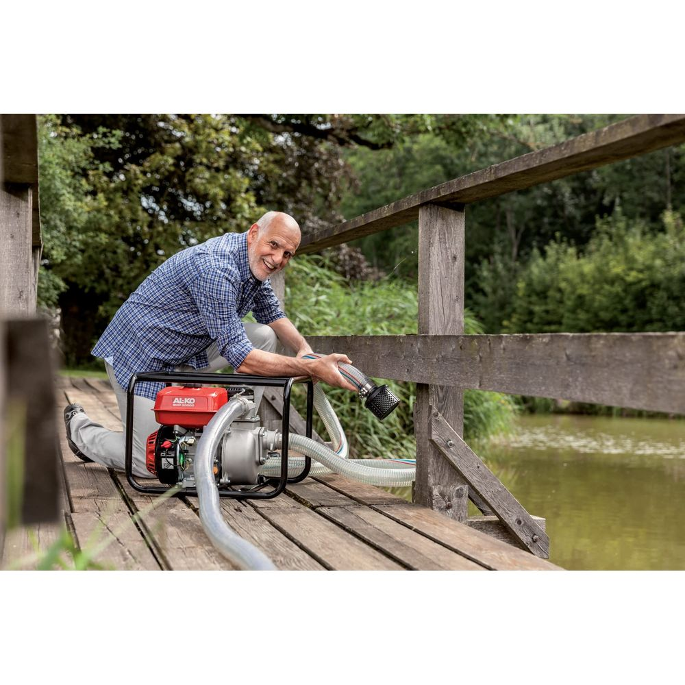 Un homme s'agenouille sur un pont en bois actionnant une pompe à eau rouge avec des tuyaux.