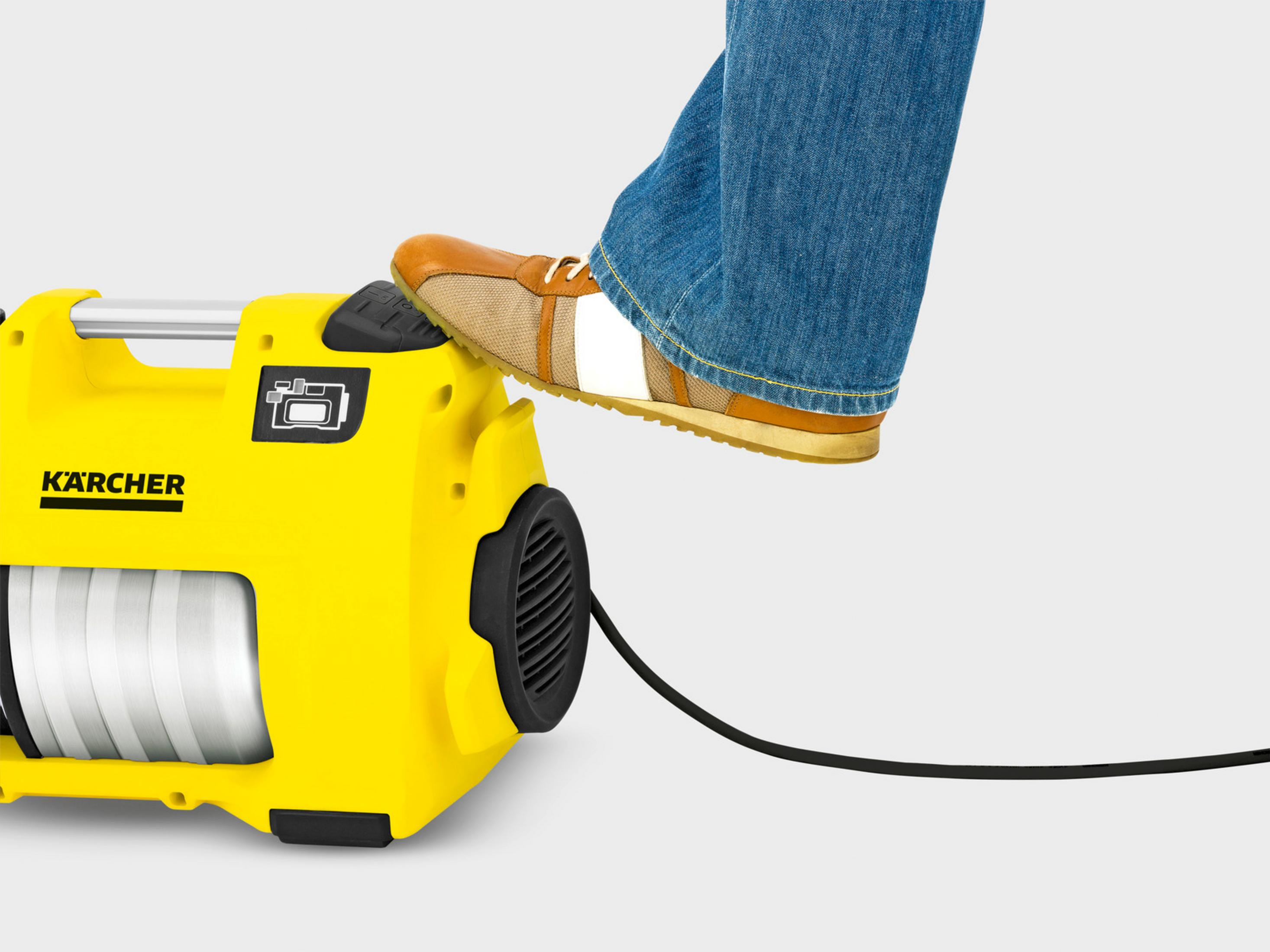 Un pie con jeans pisa una máquina Kärcher amarilla.