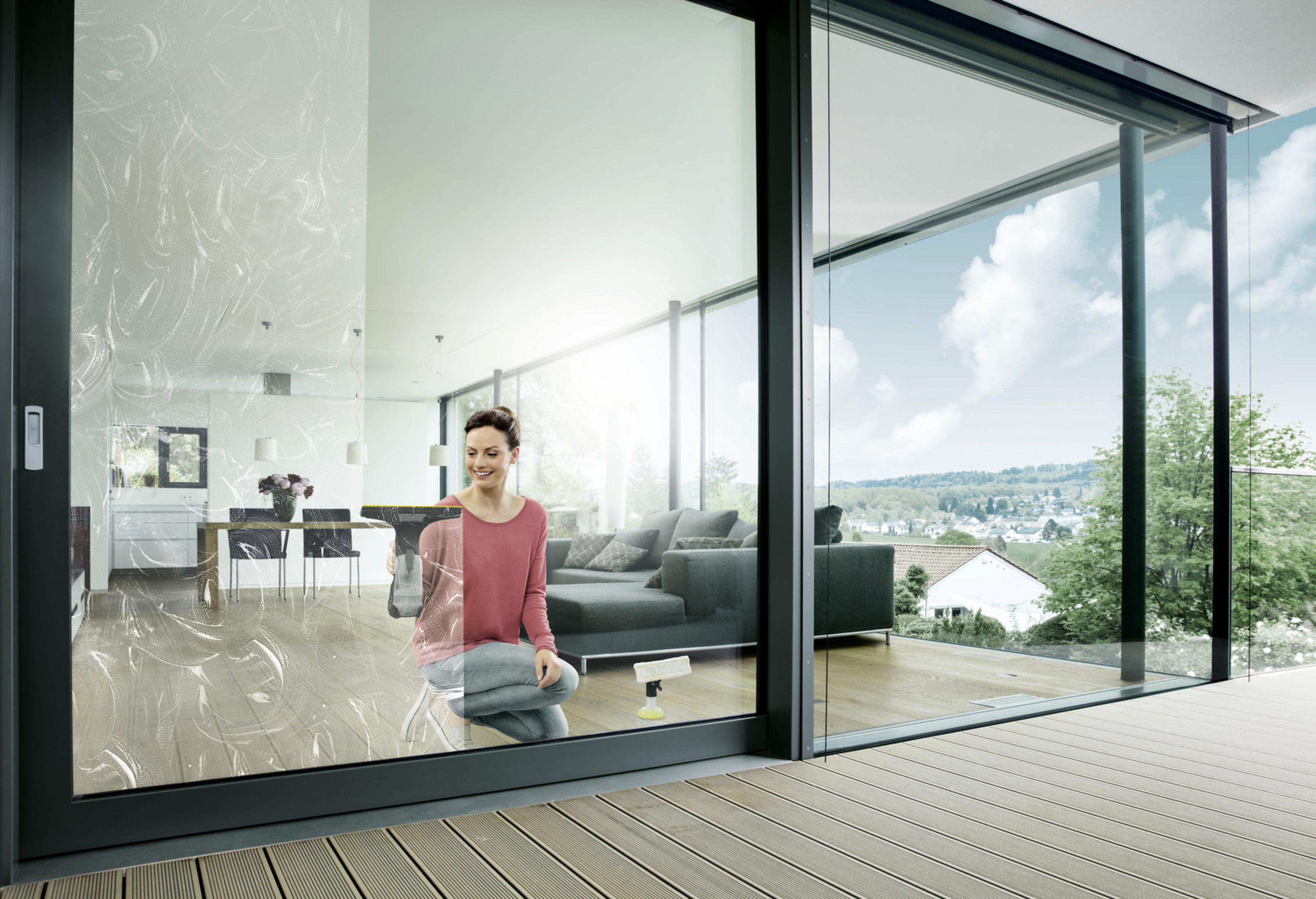 Kobieta myje okno spryskiwaczem i ściągaczką.