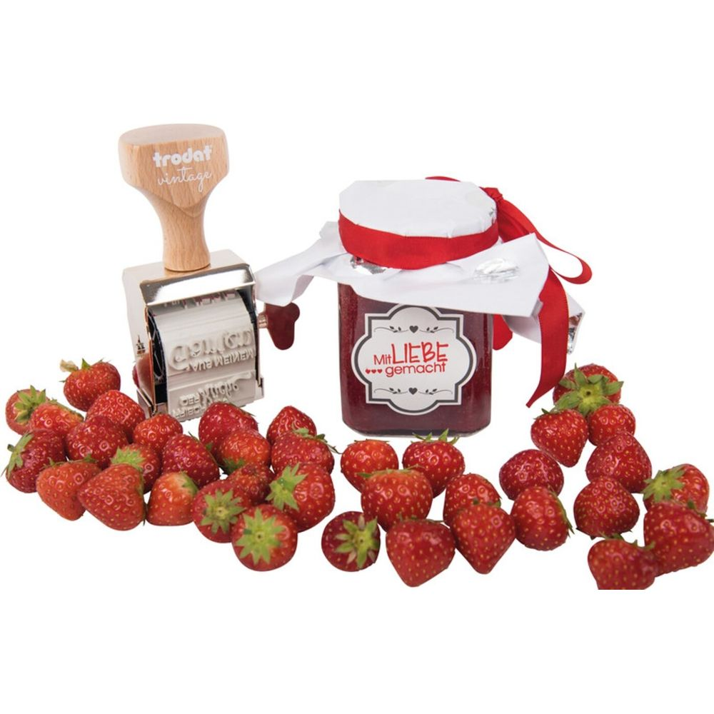 Ein Glas Erdbeermarmelade mit Stempel und vielen Erdbeeren.