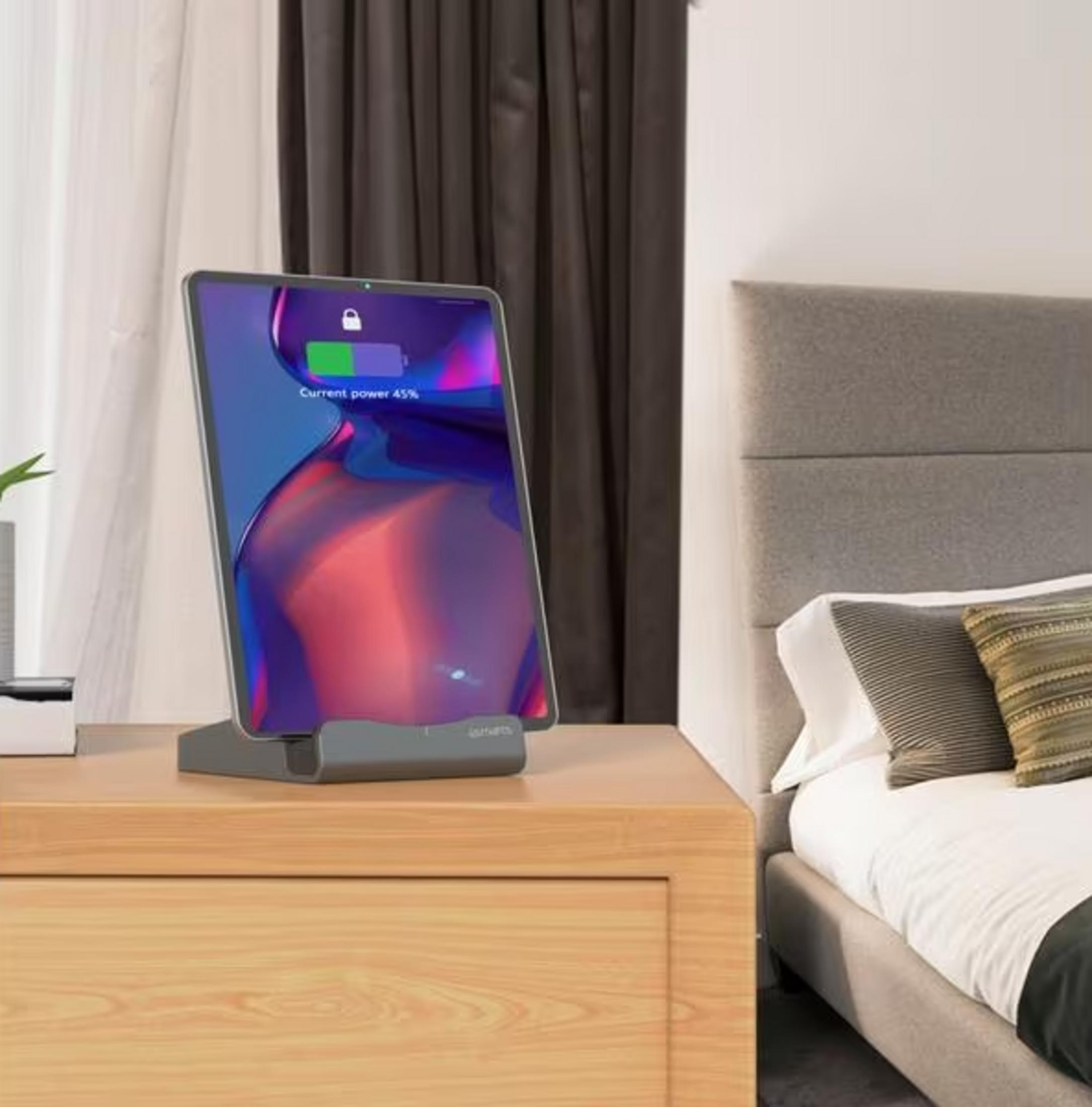 Un tablet con il 45% di batteria su un supporto grigio su un comodino accanto a un letto.