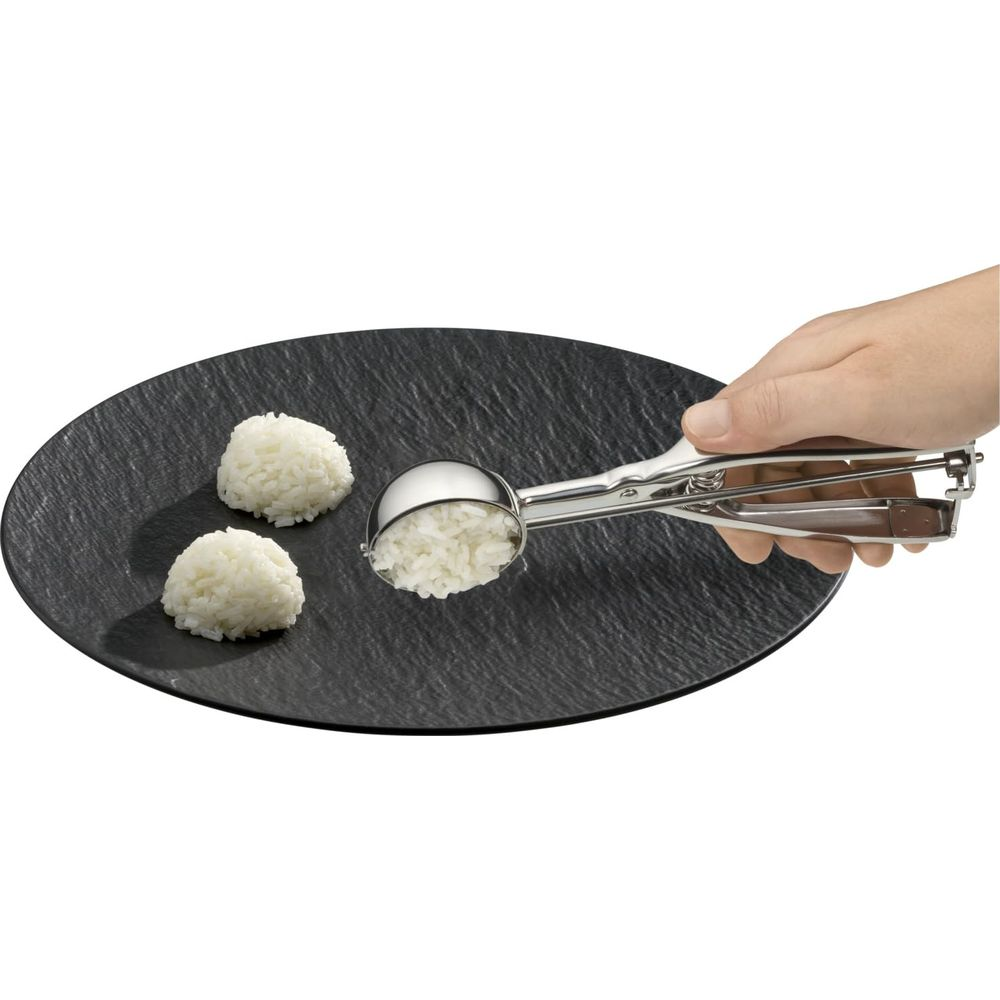 Ein Löffel mit Reis wird über einen schwarzen Teller gehalten, auf dem zwei Reisbällchen liegen.