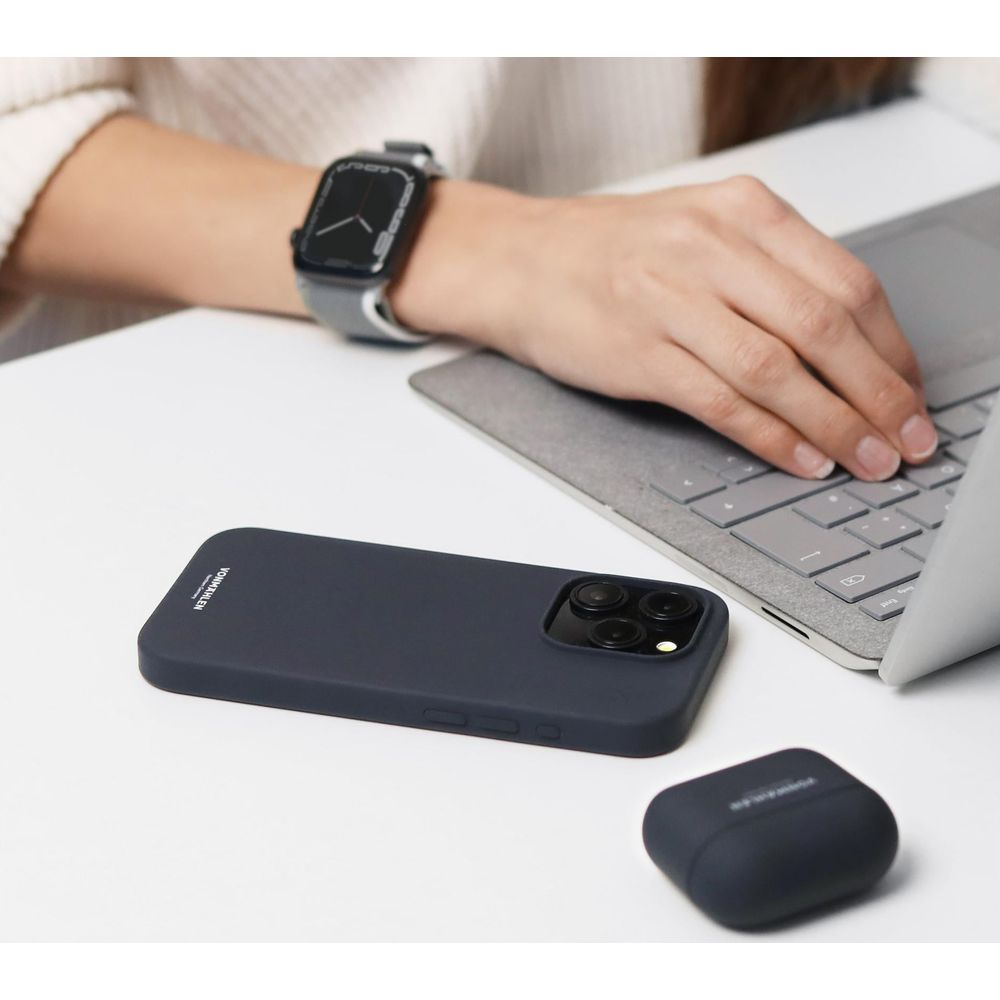 Une personne tape sur un ordinateur portable, avec un téléphone, une coque et des écouteurs à proximité.