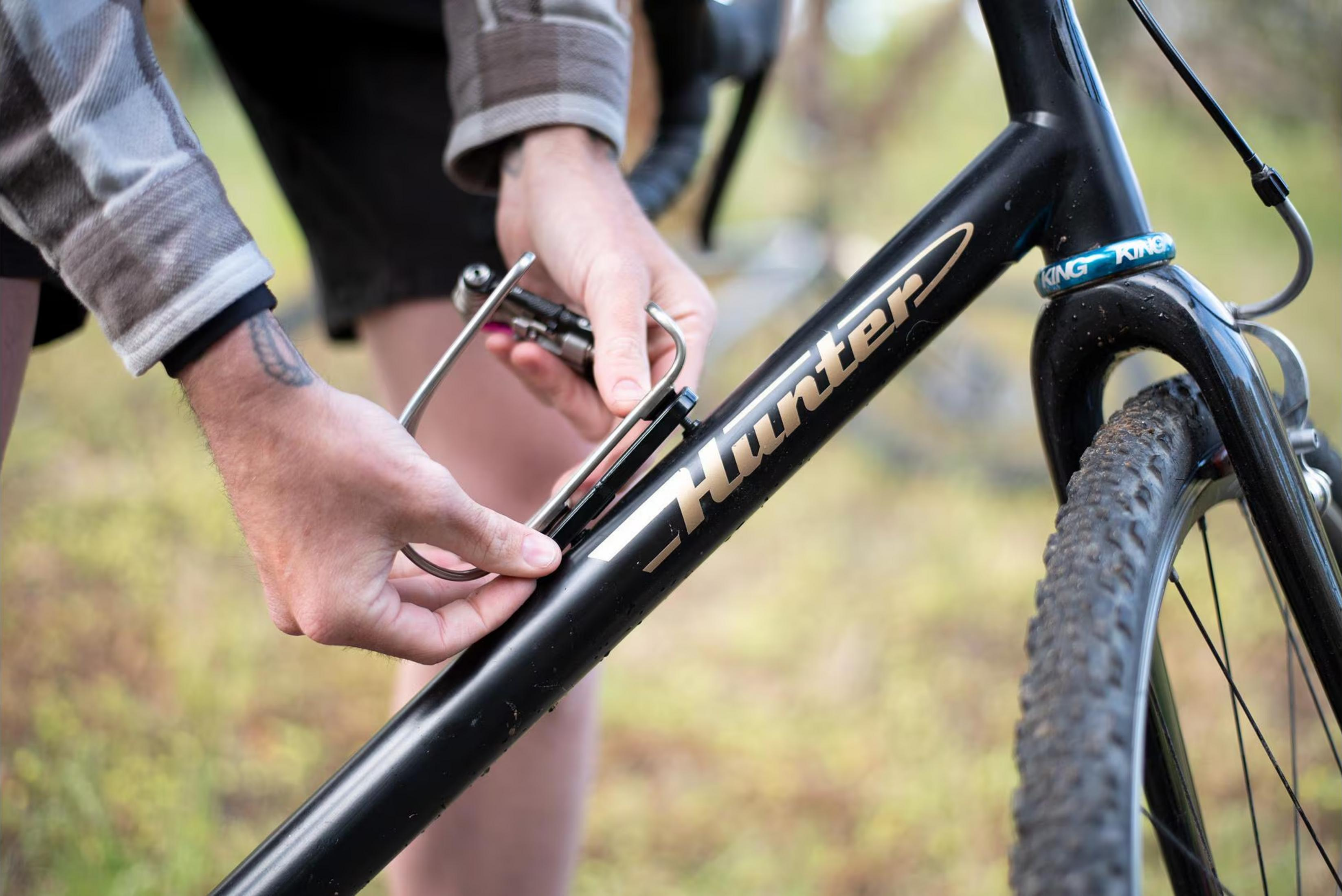 Une personne attache un outil au cadre de vélo noir avec inscription dorée.