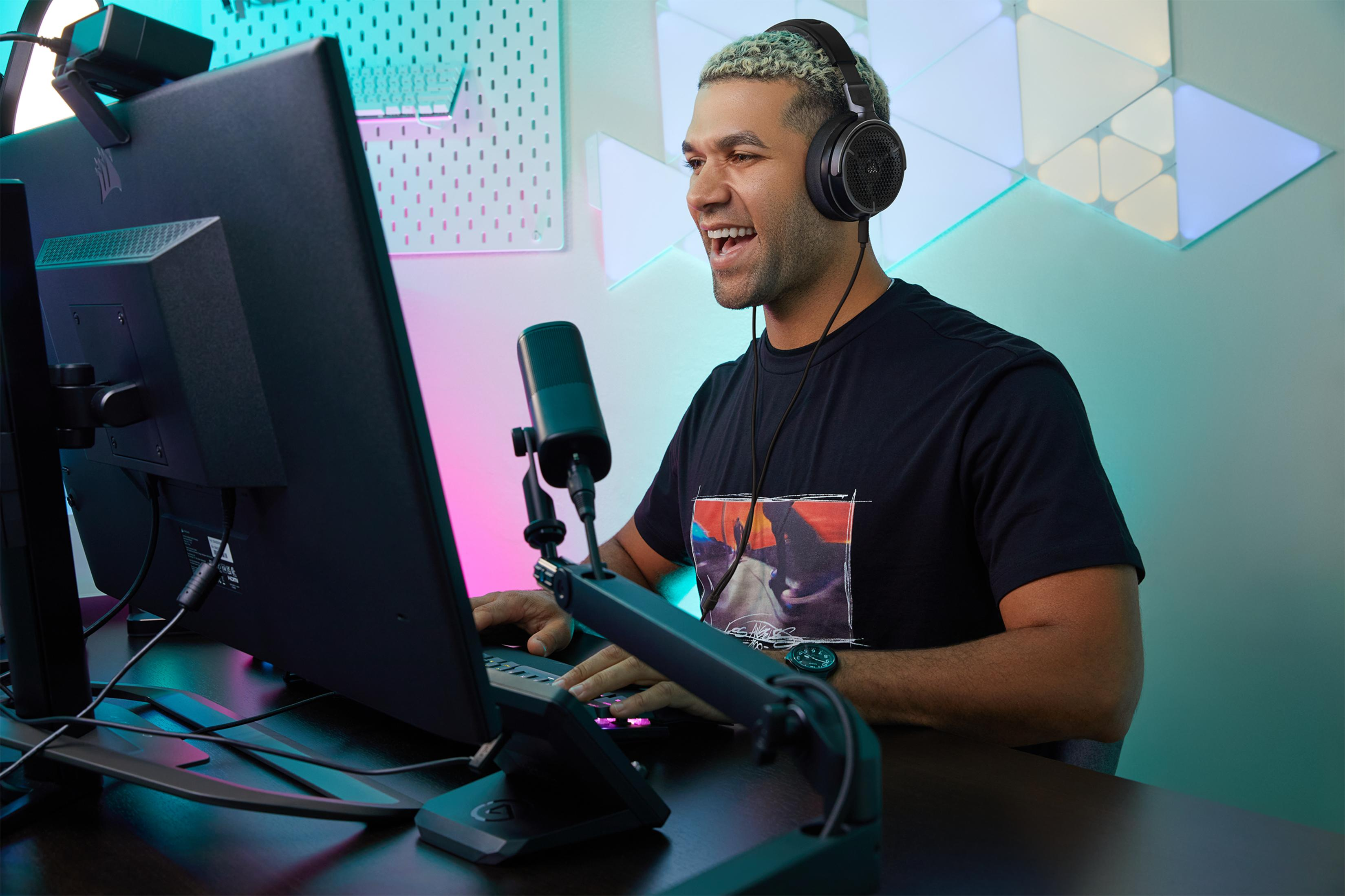Mężczyzna w słuchawkach gra na komputerze, z mikrofonem i kolorowymi światłami.