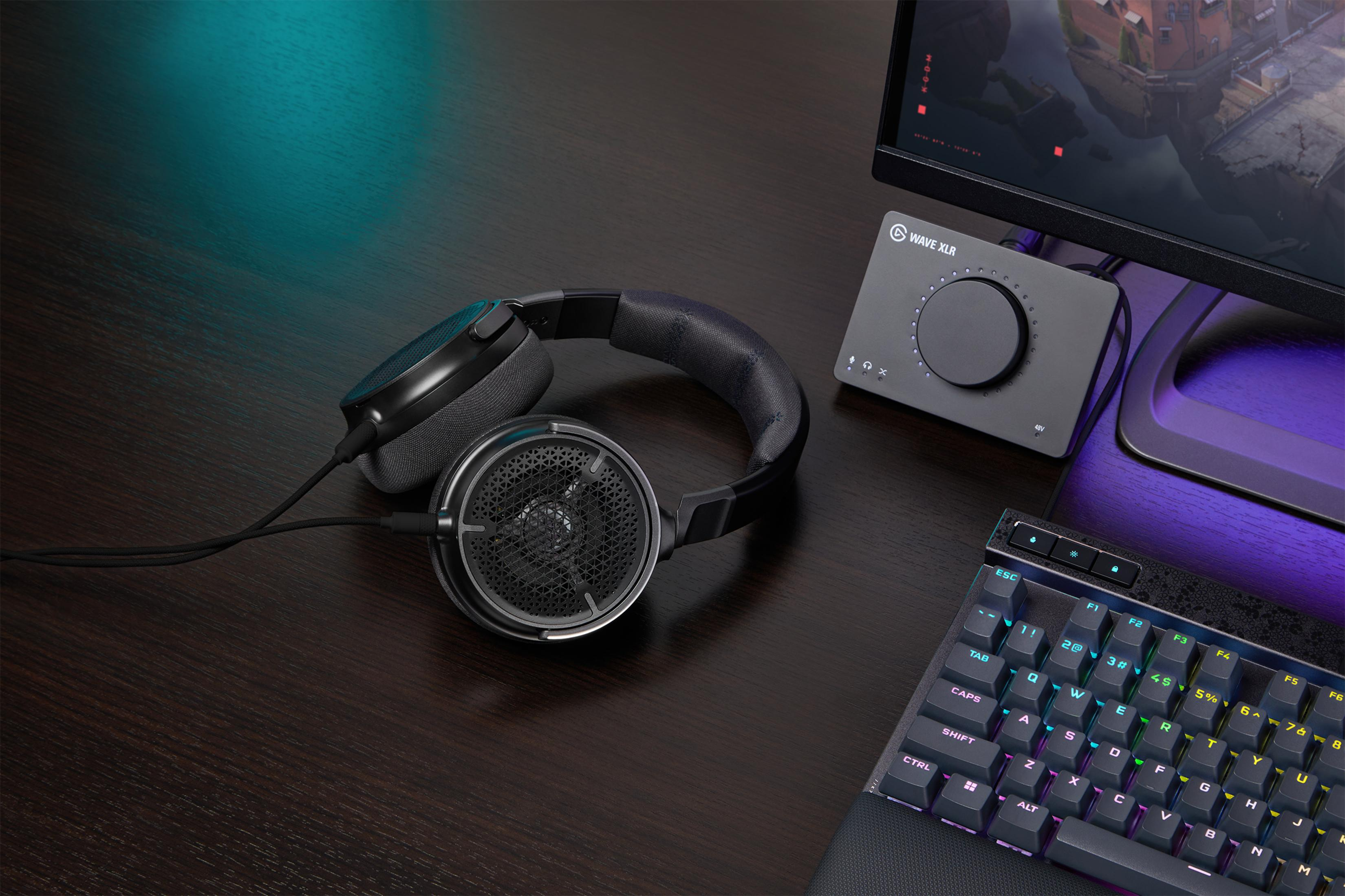 Słuchawki, mikrofon i klawiatura na ciemnym biurku.