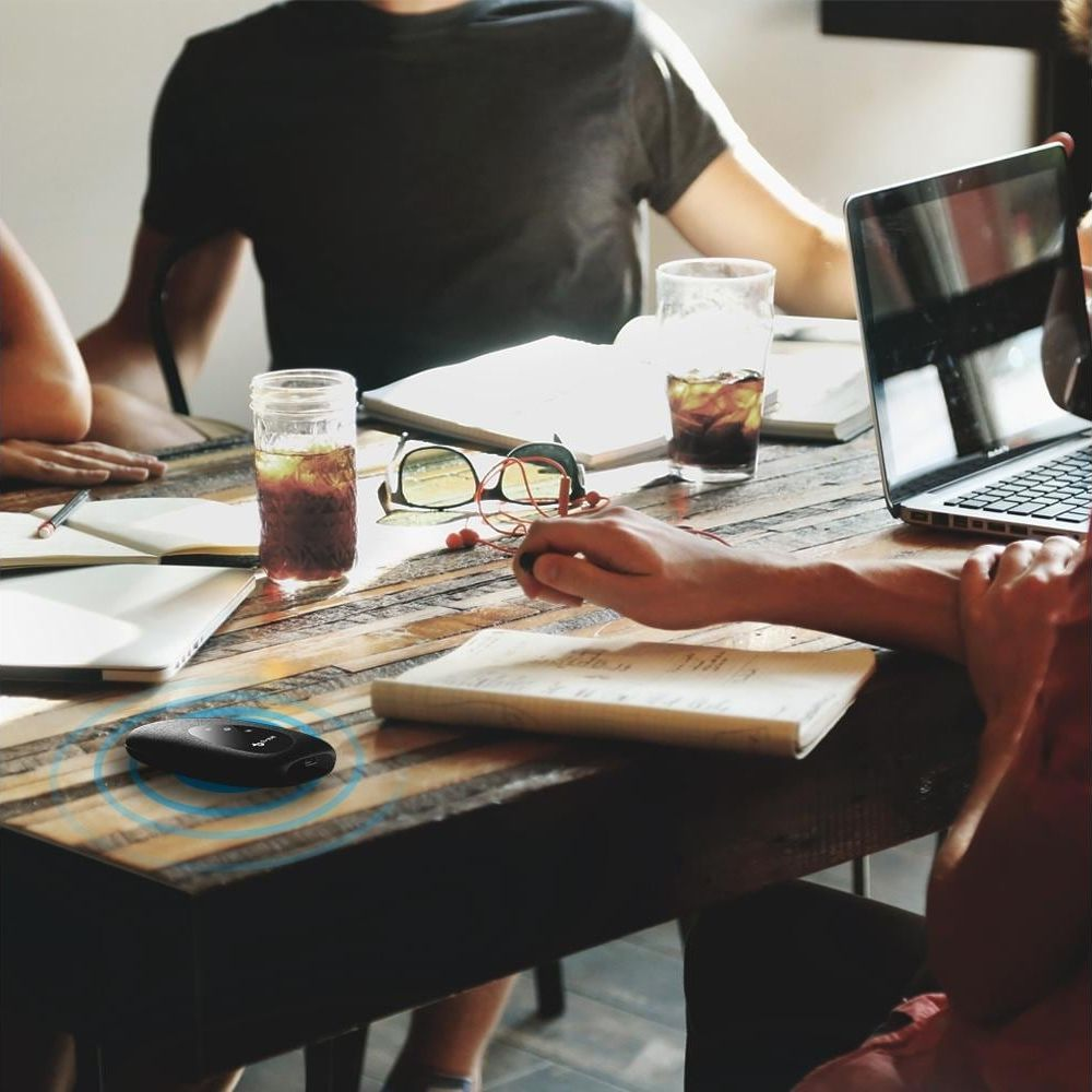 Un gruppo di persone siede a un tavolo di legno con bevande, libri e un laptop.