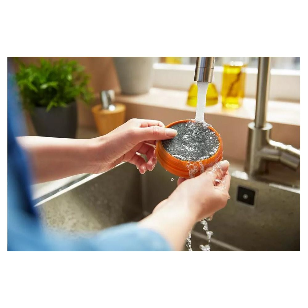 Ręce płuczą okrągły, pomarańczowy filtr pod bieżącą wodą w zlewie.