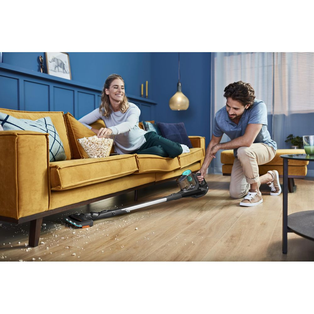 Mężczyzna odkurza podłogę, kobieta siedzi na kanapie z popcornem.