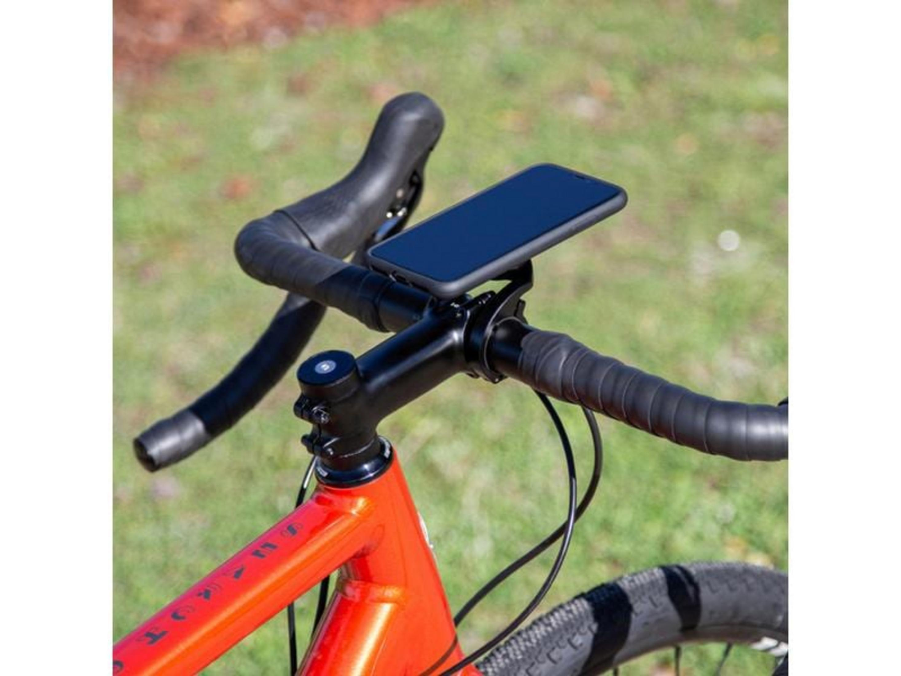 Ein Smartphone ist auf dem Lenker eines roten Fahrrads montiert. Gras im Hintergrund.