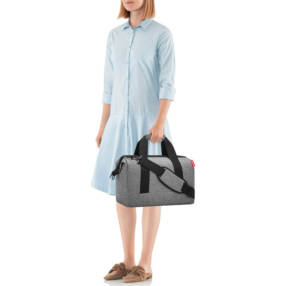 Una donna in abito azzurro tiene una borsa grigia con cinghie nere.