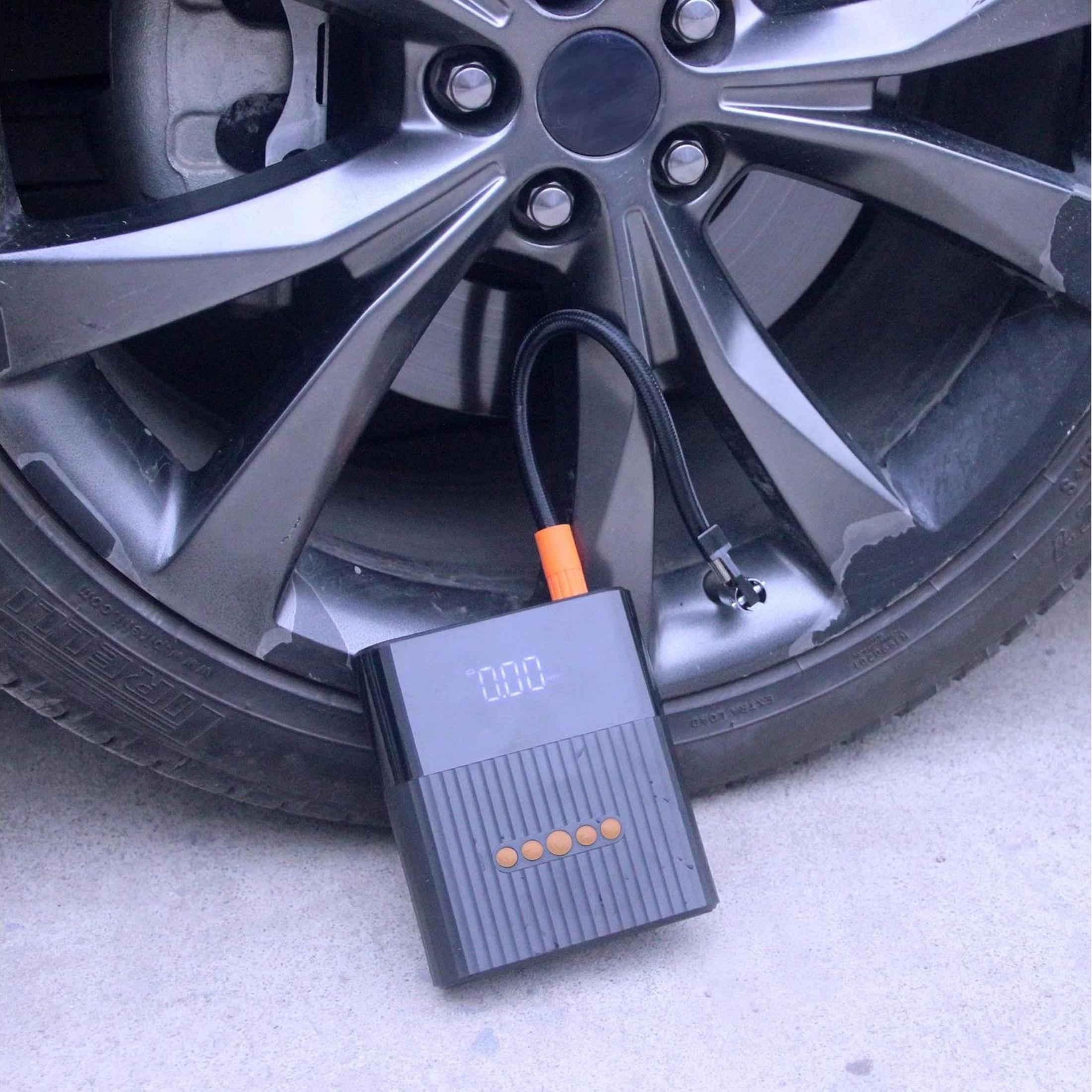 Un gonfiatore portatile per pneumatici con tubo giace accanto a una ruota d'auto.