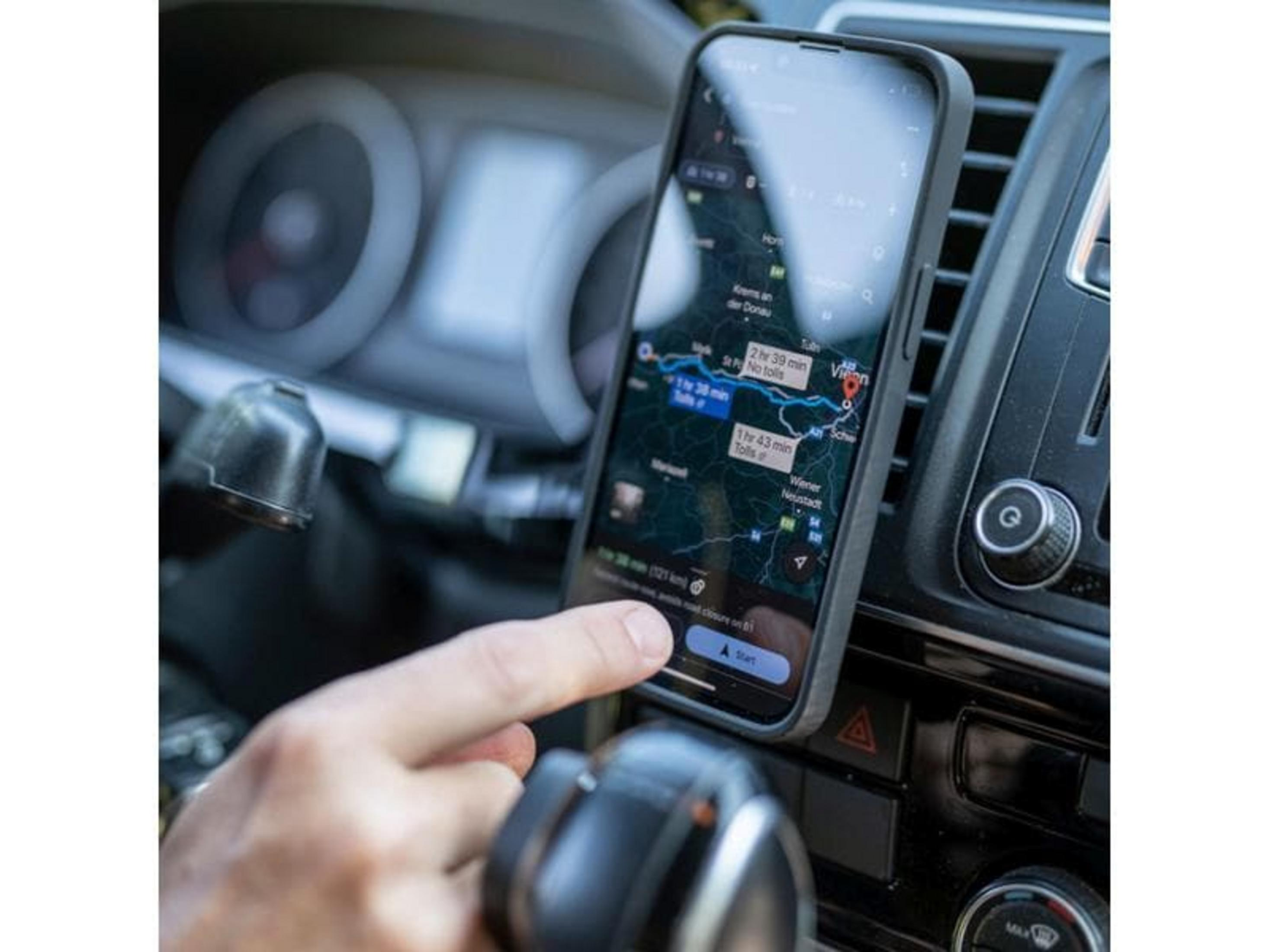 Eine Hand tippt auf eine Navigations-App auf einem Smartphone im Auto.