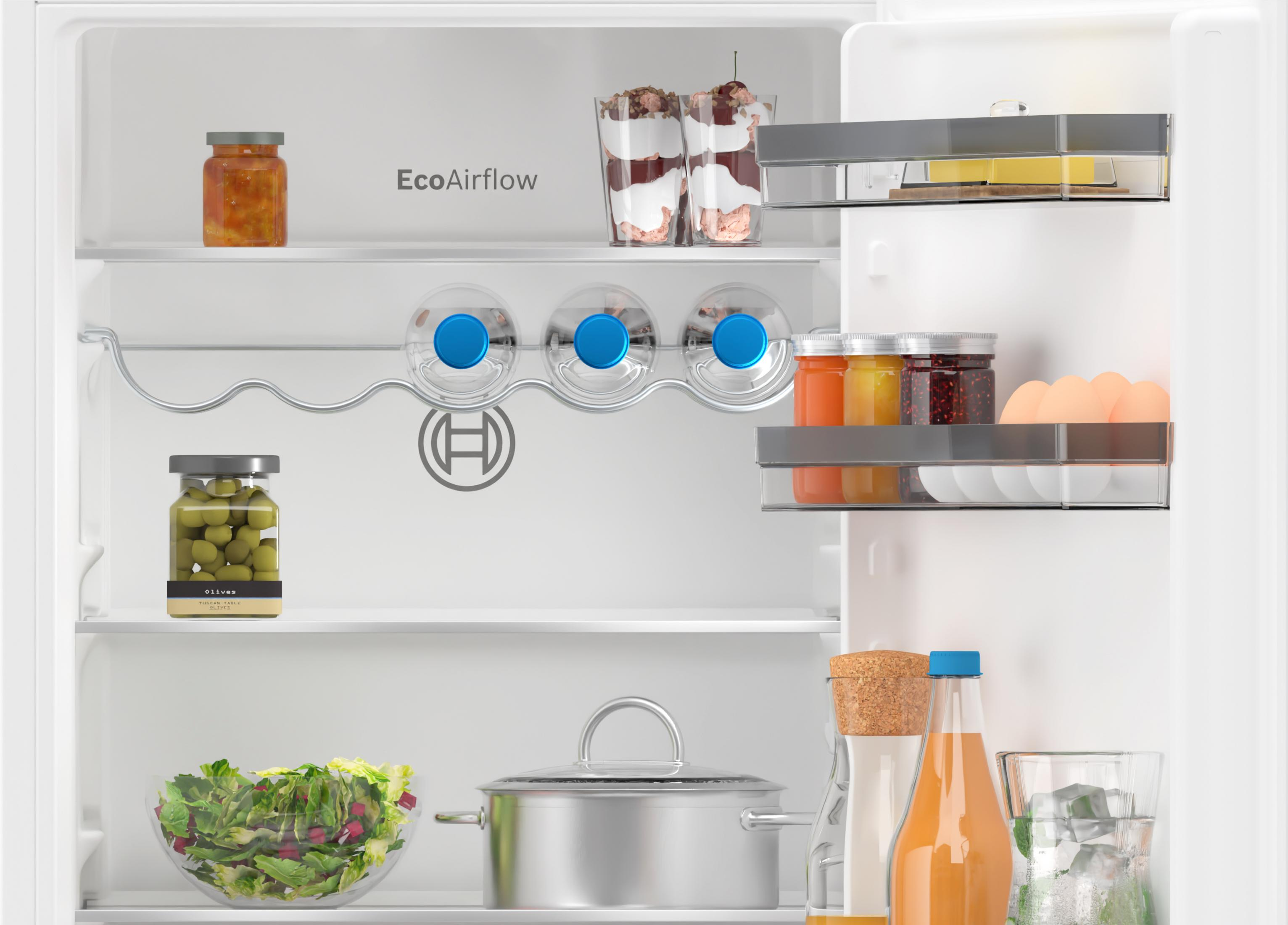 Otwarta lodówka z słoikami, oliwkami, jajkami, sałatką i deserami.