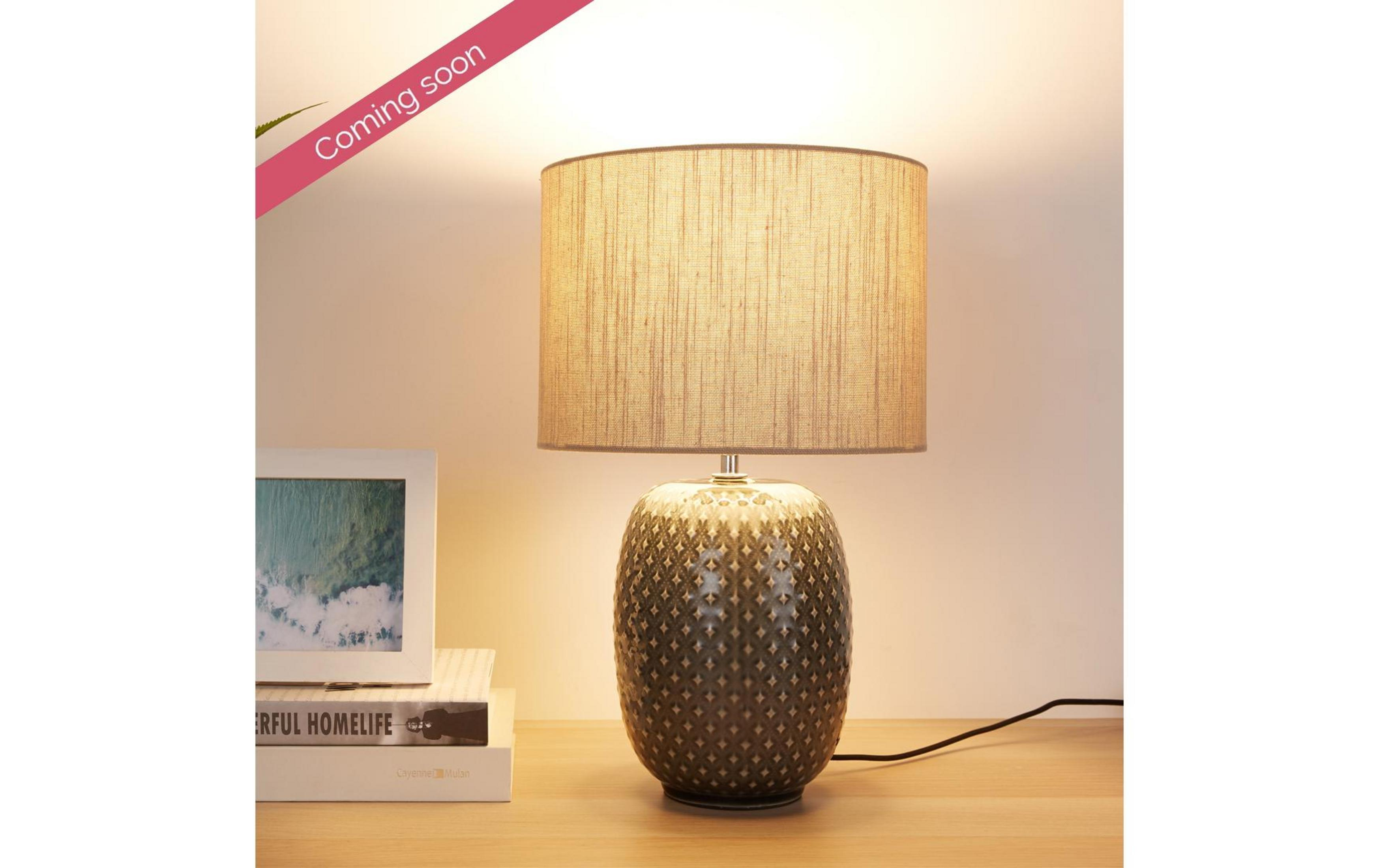 Szara lampa z wzorem stoi na drewnianym stole obok książek.