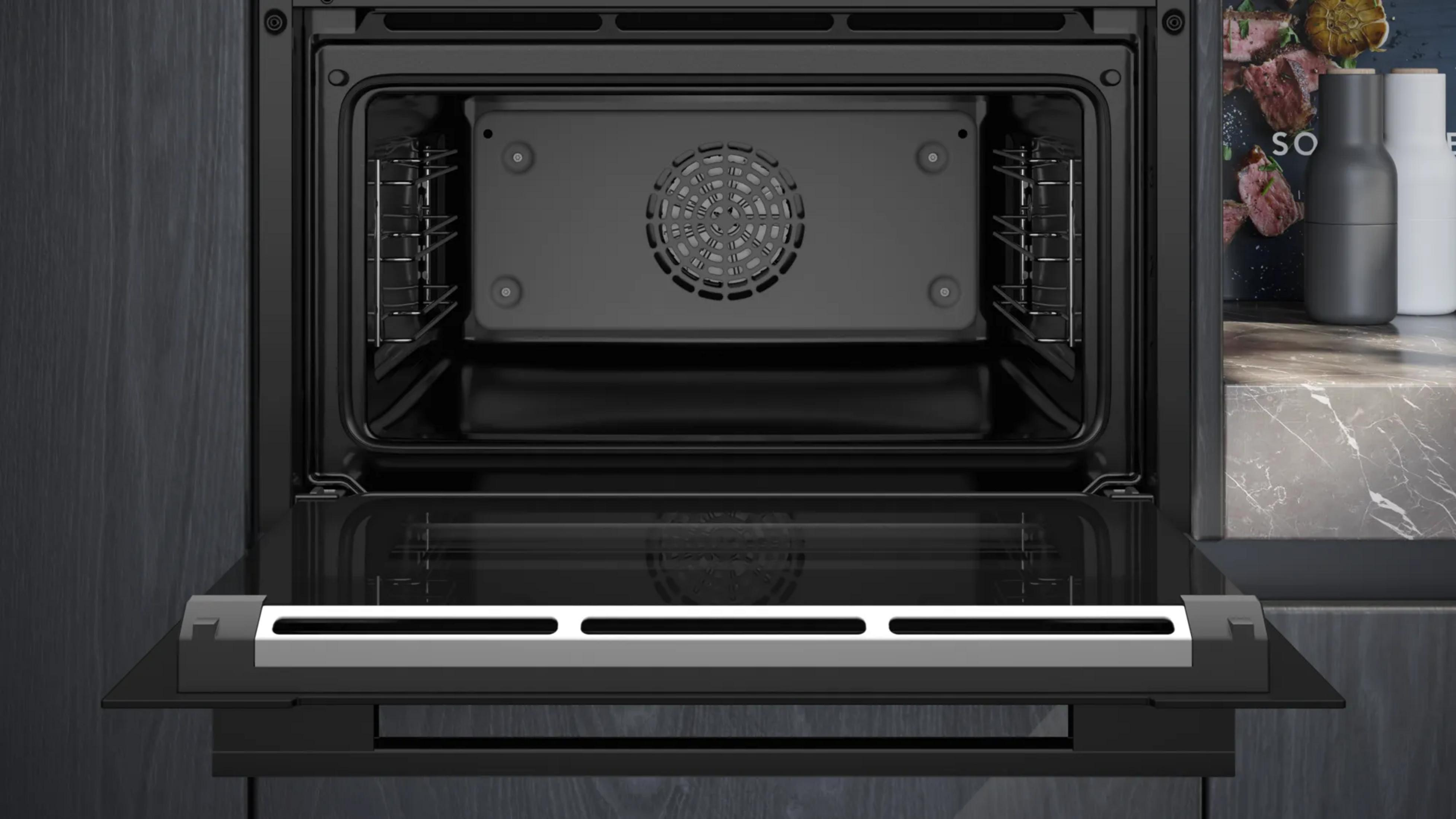 Un four encastrable noir ouvert avec grill et ventilateur. À côté, des salières et un livre de cuisine.