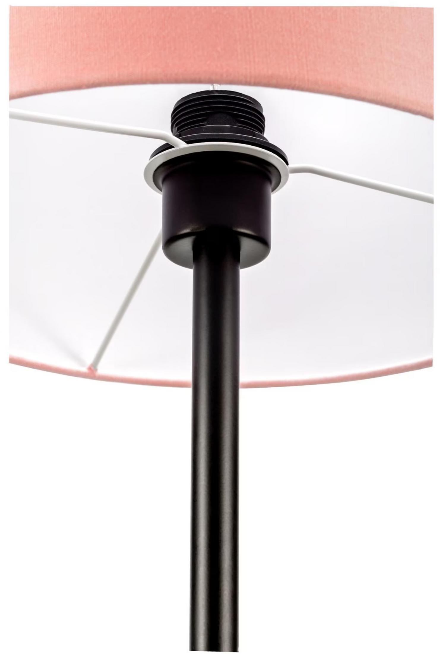 Zbliżenie podstawy lampy z różowym abażurem i ciemnym słupkiem.