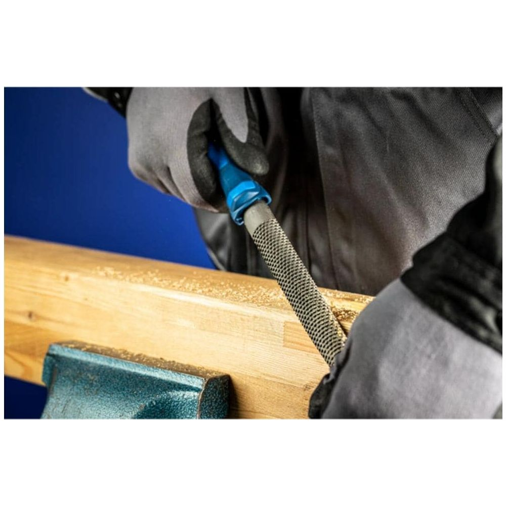 Hände mit Handschuhen feilen an Holz in einem Schraubstock. Holzspäne liegen herum.
