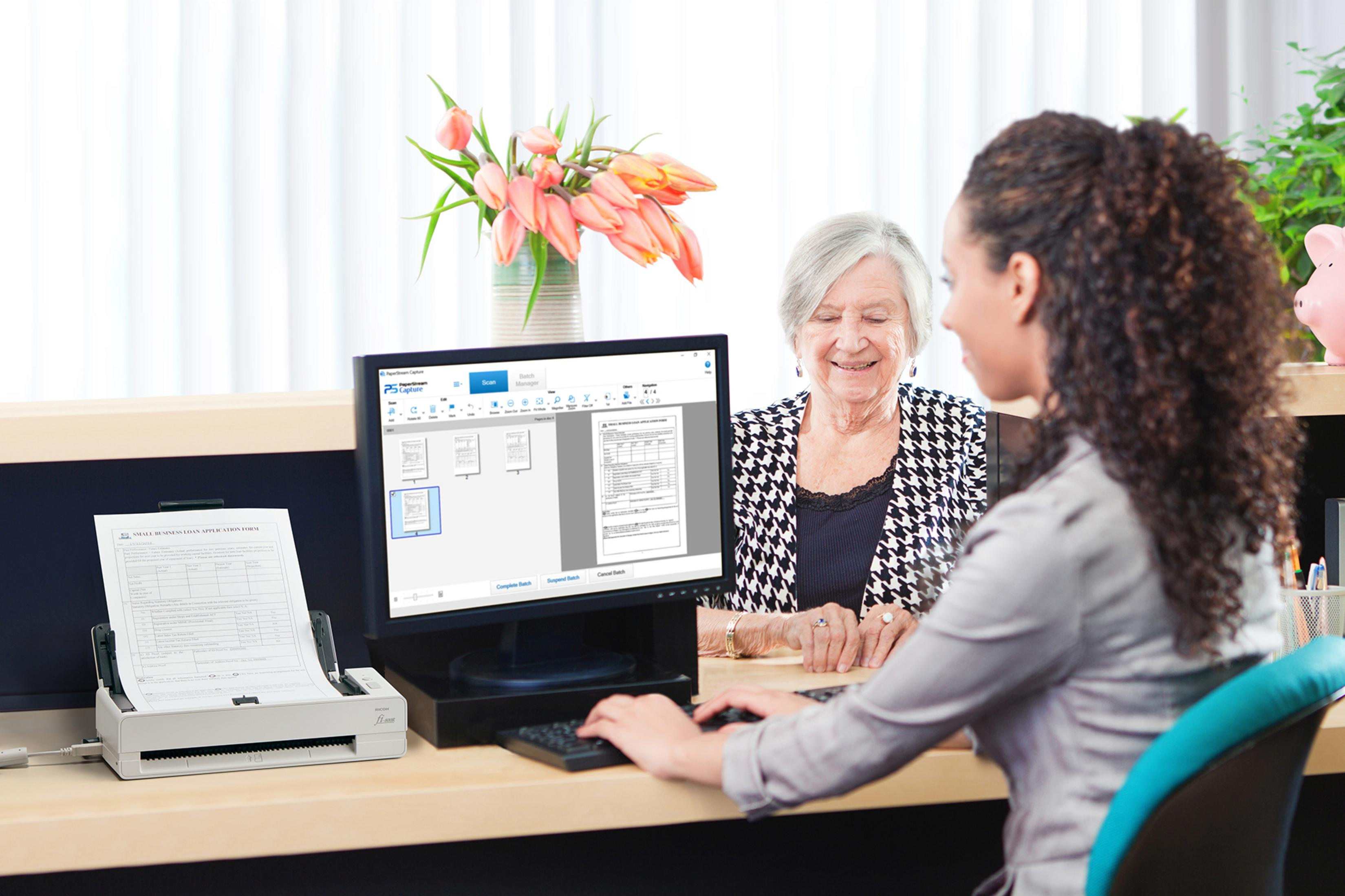 Dwie kobiety przy biurku ze skanerem i komputerem.