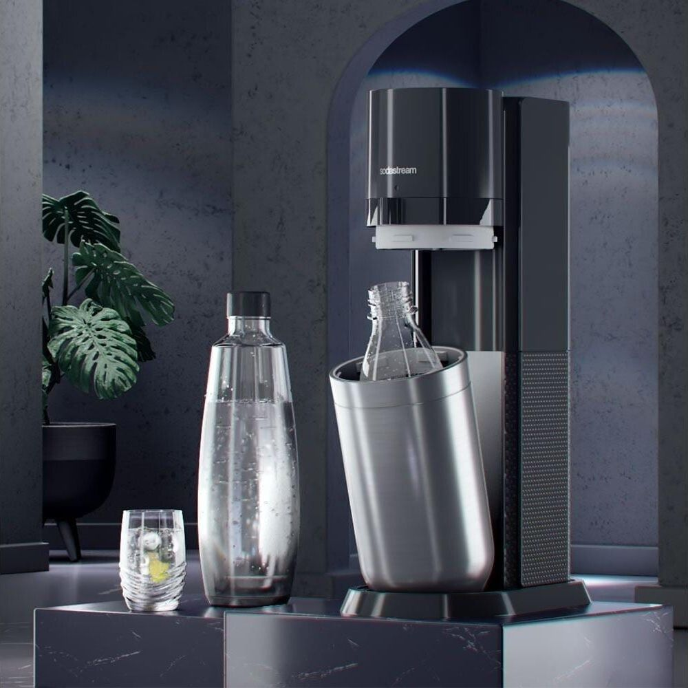 Una macchina SodaStream con bottiglie e un bicchiere su marmo scuro.