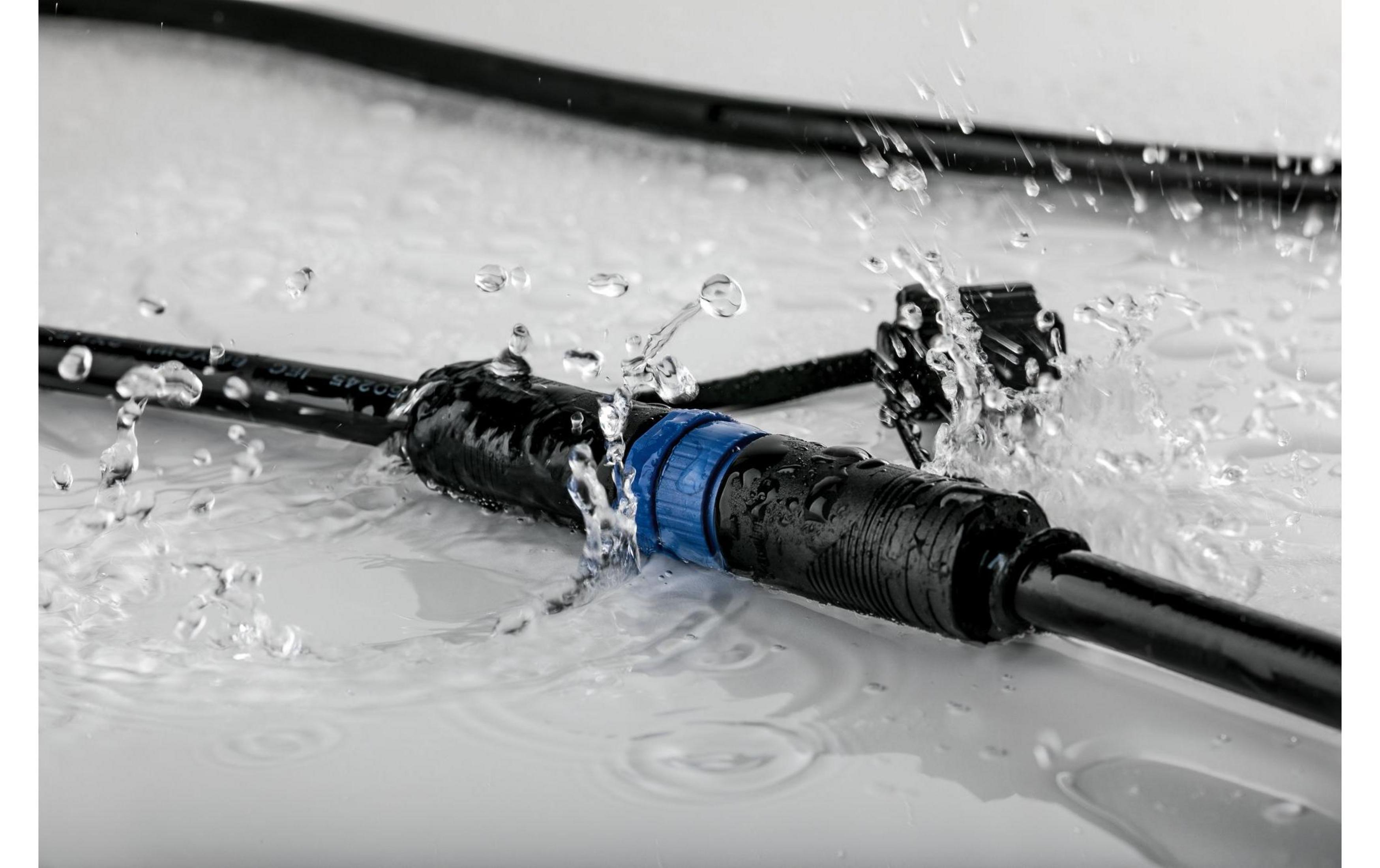 Schwarze Kabelstecker mit blauen Ringen in Wasser, Spritzer bilden sich.