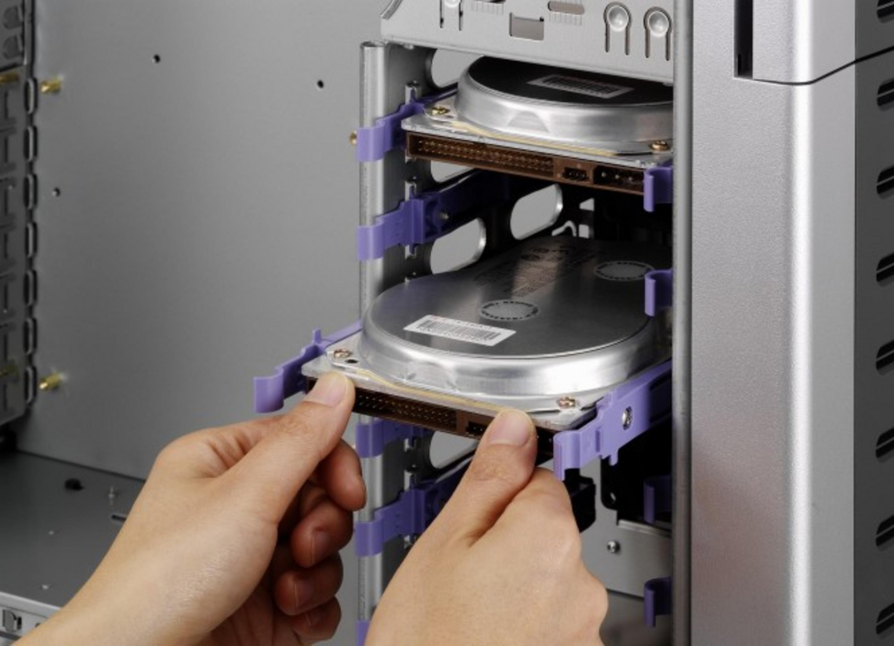 Ręce instalują dysk twardy w srebrnej obudowie komputera z fioletowymi uchwytami.
