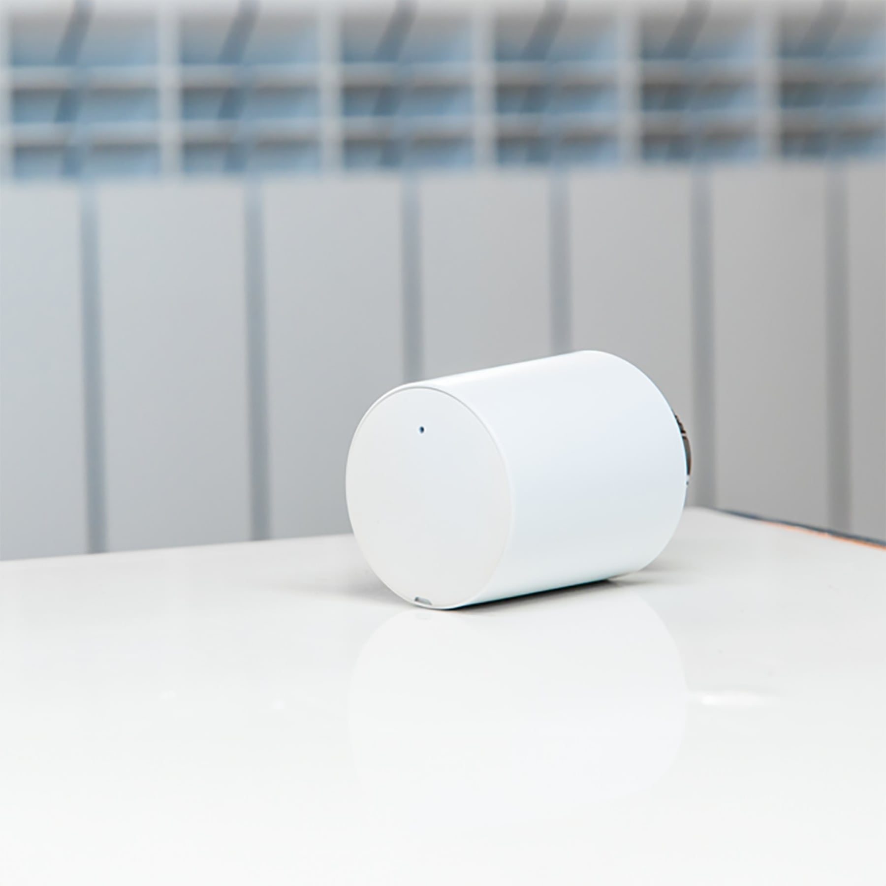 Biały, cylindryczny przedmiot z małą niebieską kropką leży na białej powierzchni.