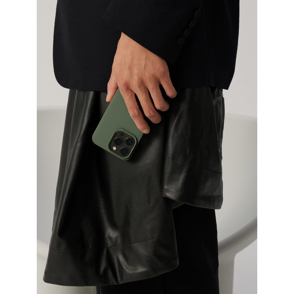 Eine Hand hält eine grüne Handyhülle mit Dreifachkamera. Die Person trägt einen schwarzen Blazer über einem schwarzen Lederrock.