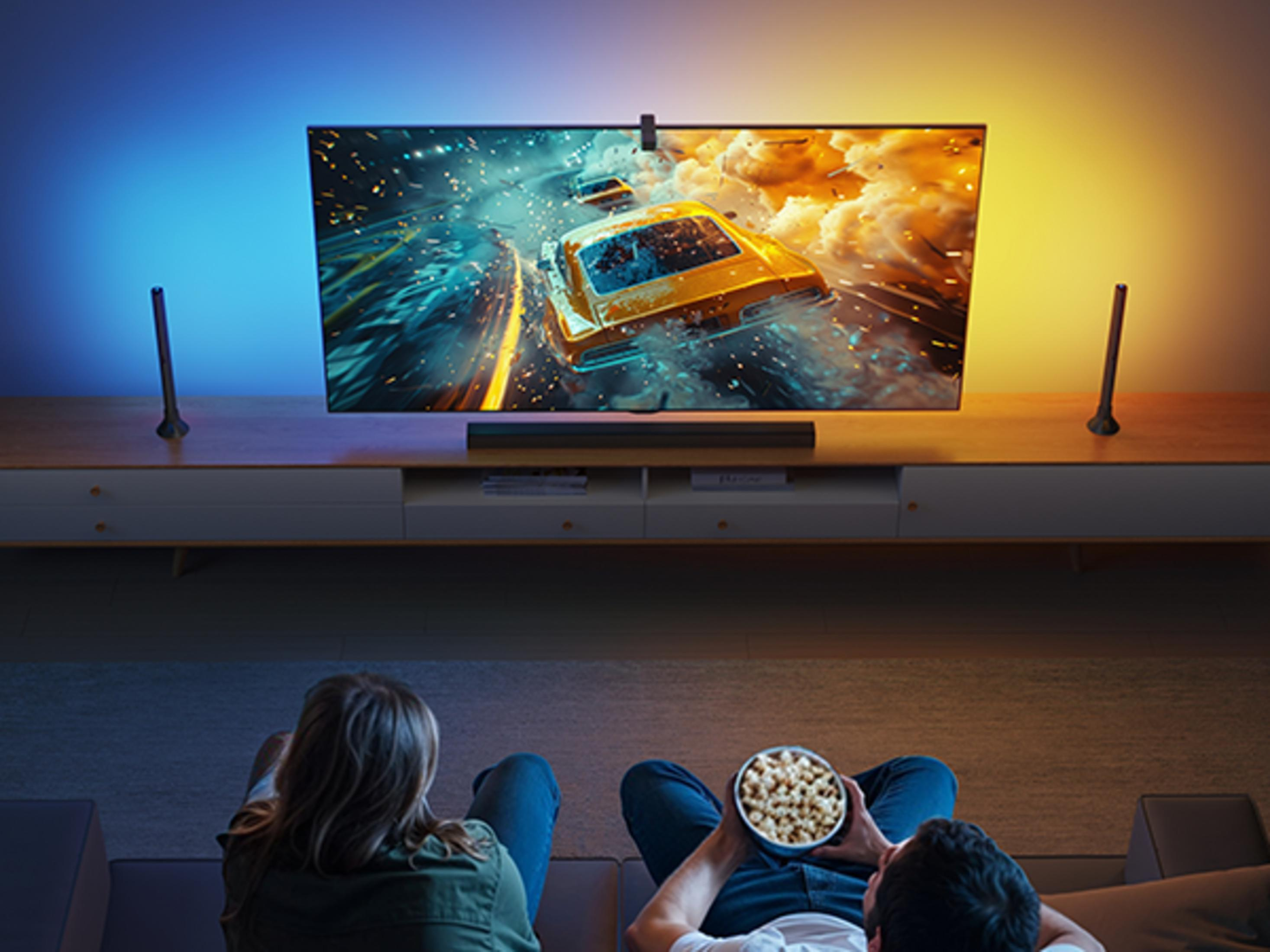 İki kişi TV izliyor, biri patlamış mısır yiyor. TV'de araba yarışı var.