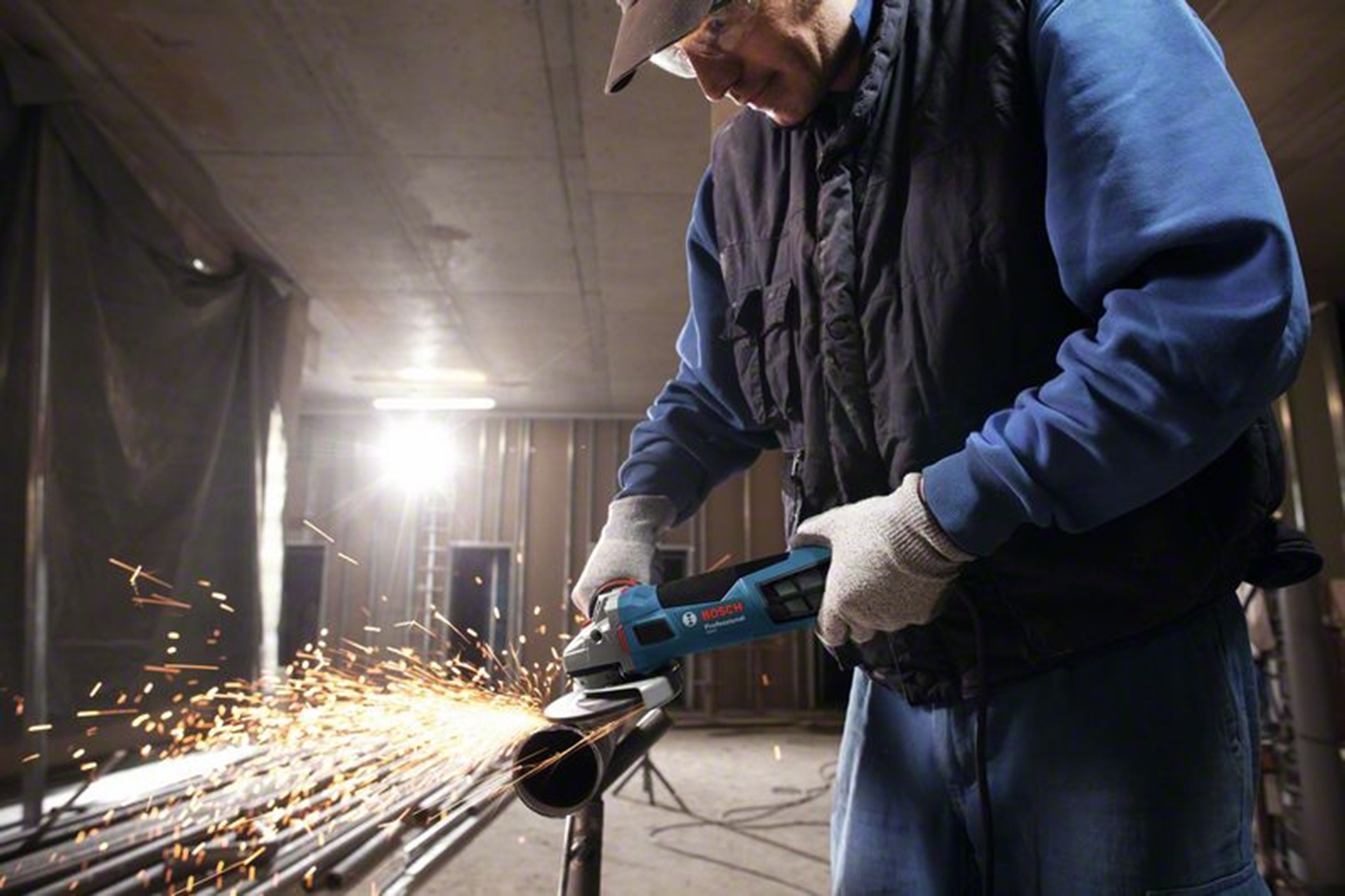 Un homme portant des lunettes de sécurité meule des tuyaux avec une meuleuse d'angle, des étincelles jaillissent.