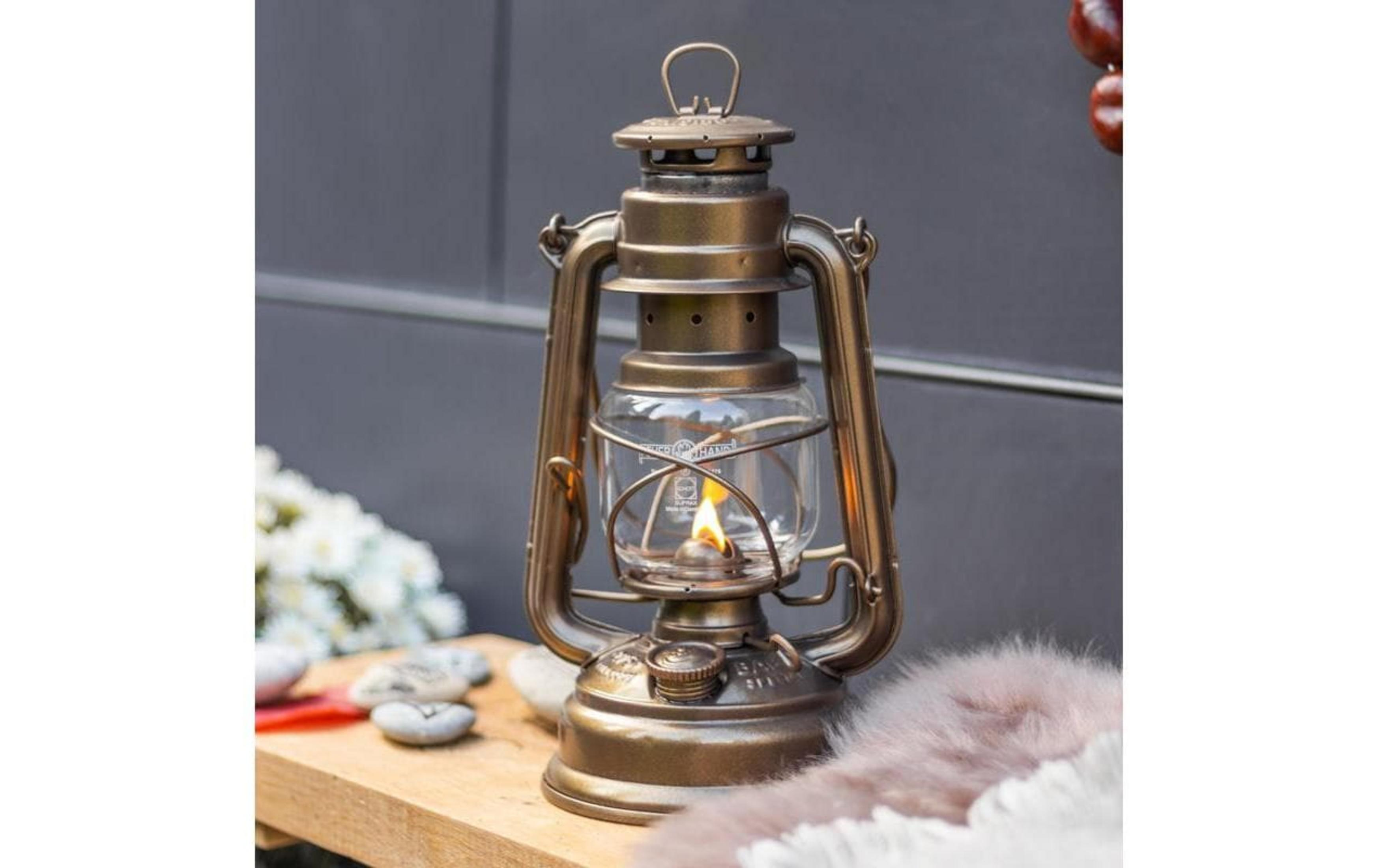 Eine bronzefarbene Laterne mit brennender Flamme steht auf einem Holztisch.