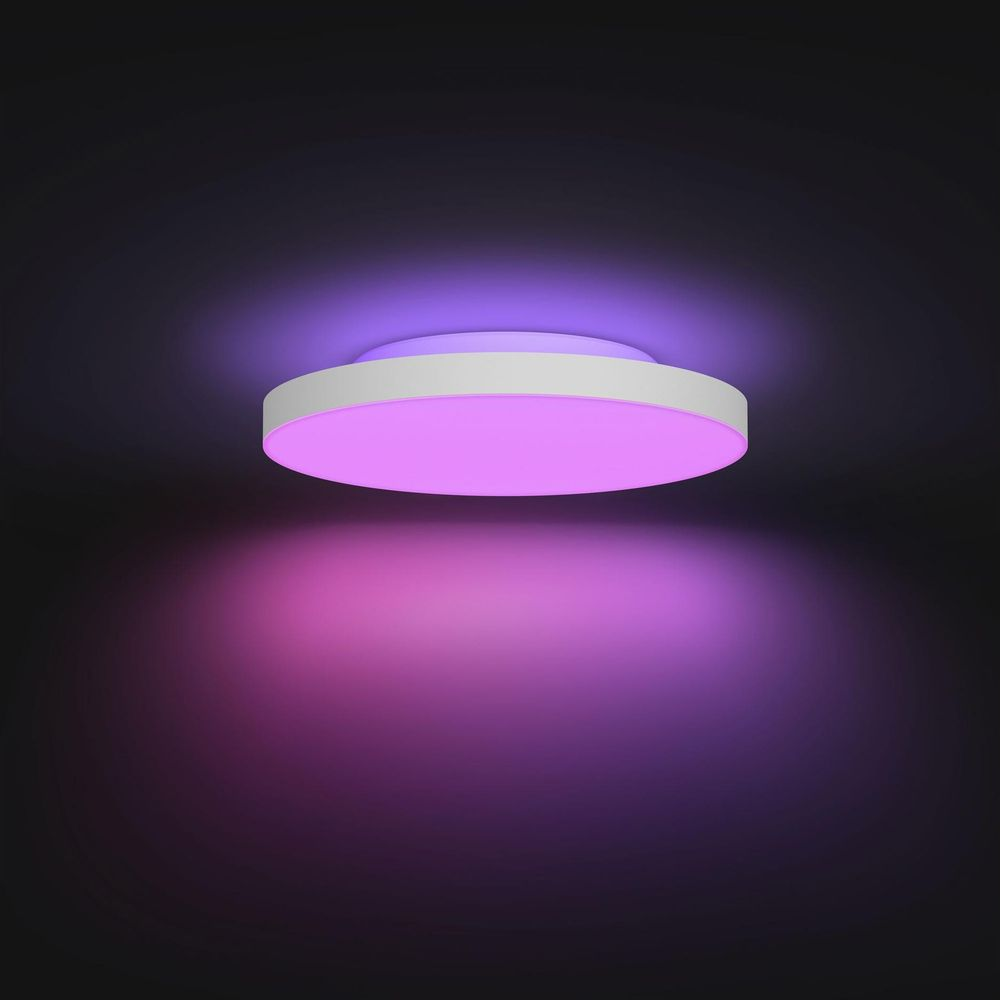 Biała lampa sufitowa emituje różowe i fioletowe światło na ciemnym tle.