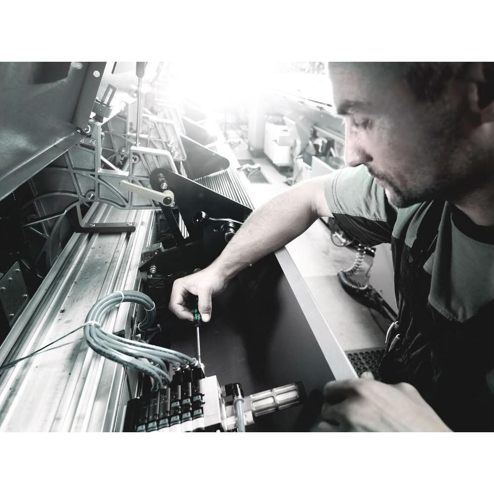 Mężczyzna naprawia maszynę śrubokrętem; widoczne są kable i części.