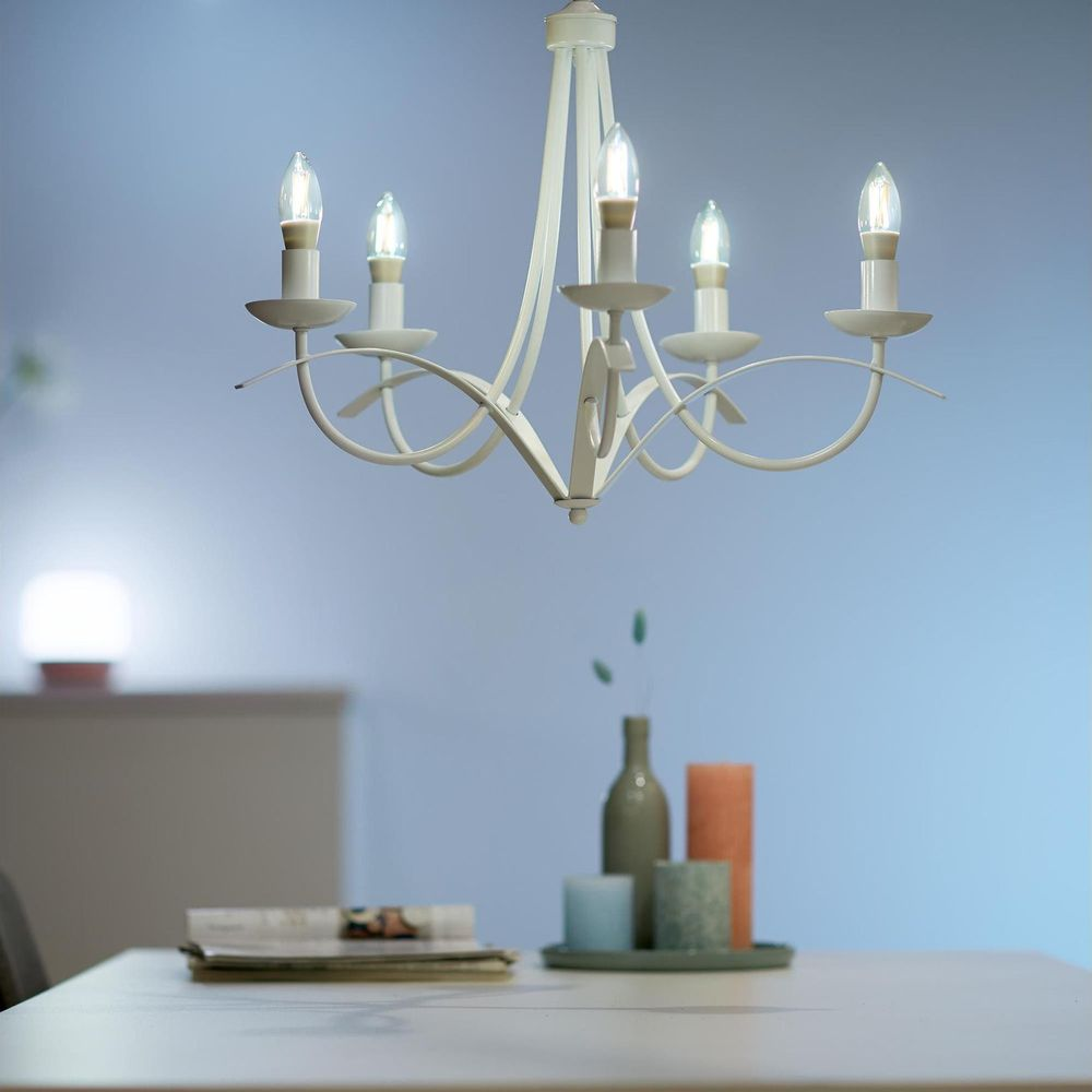Un lustre blanc au-dessus d'une table avec des bougies, une bouteille et des magazines.