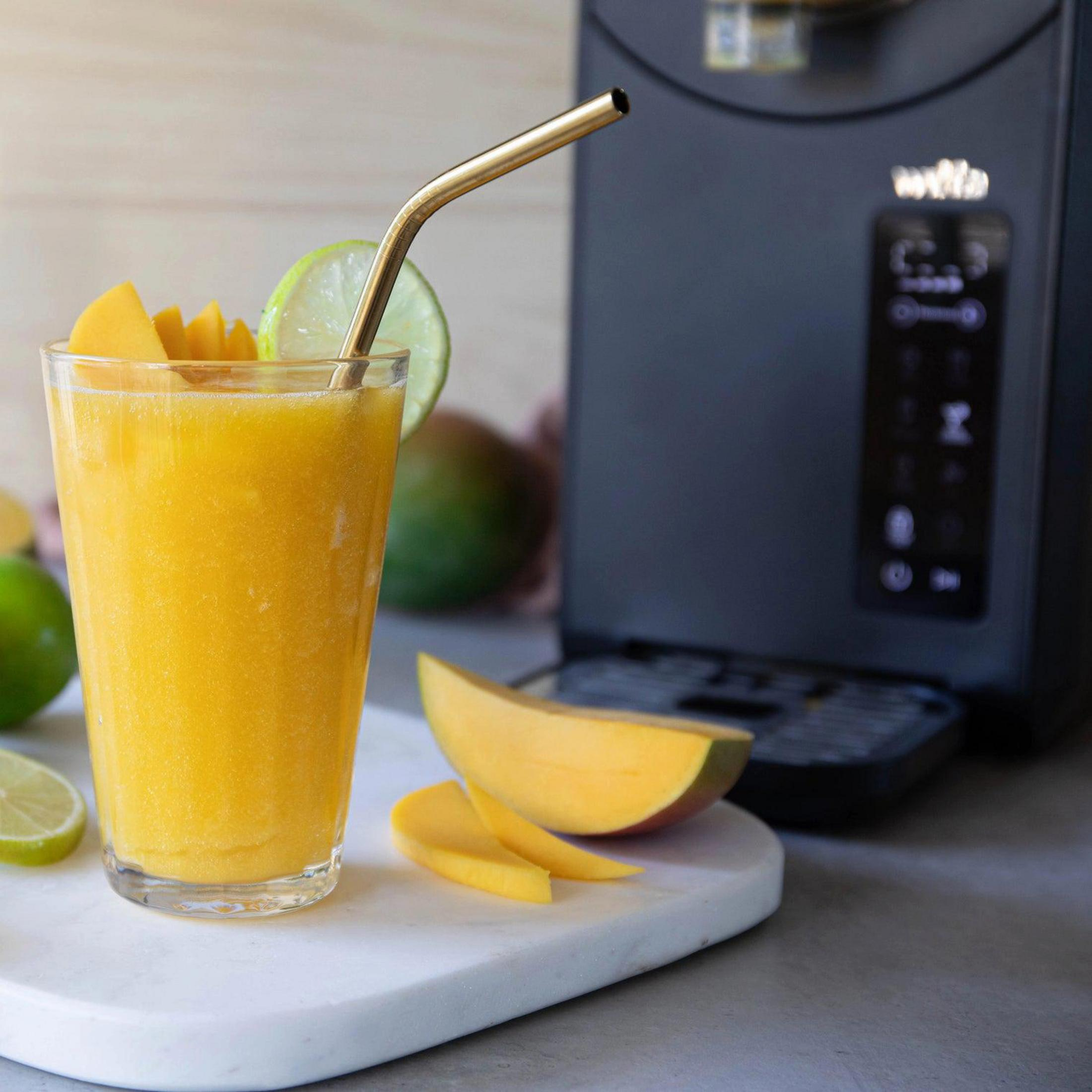 Un bicchiere di frullato mango-lime con pezzi di frutta e cannuccia dorata.