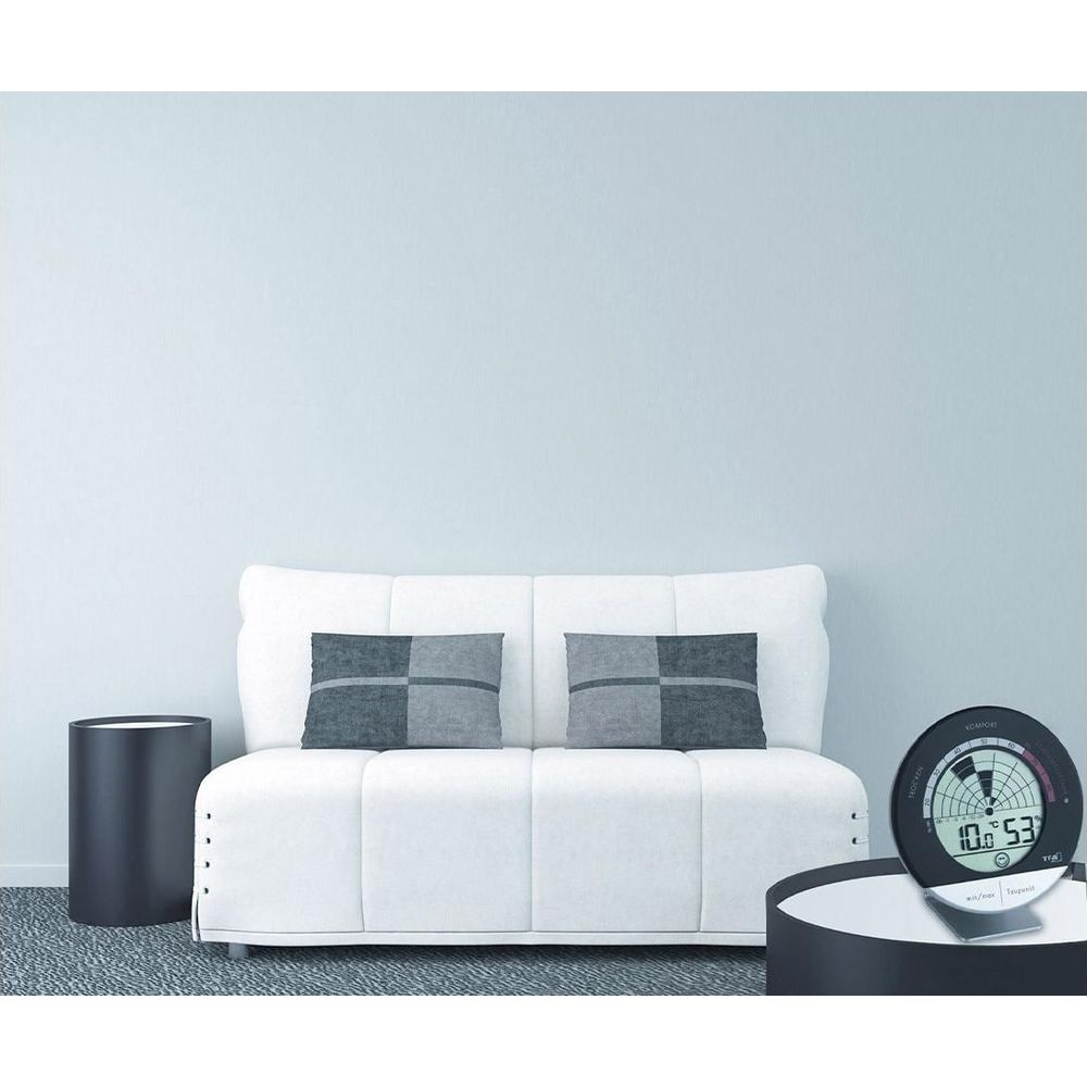 Ein weies Sofa mit grauen Kissen steht vor einer hellblauen Wand. Daneben ein schwarzer Beistelltisch.