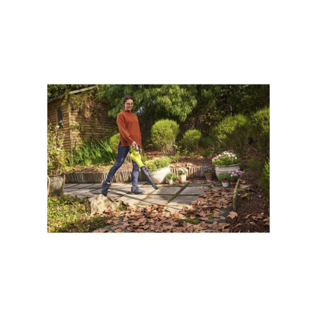 Donna con soffiatore nel giardino, foglie autunnali a terra.